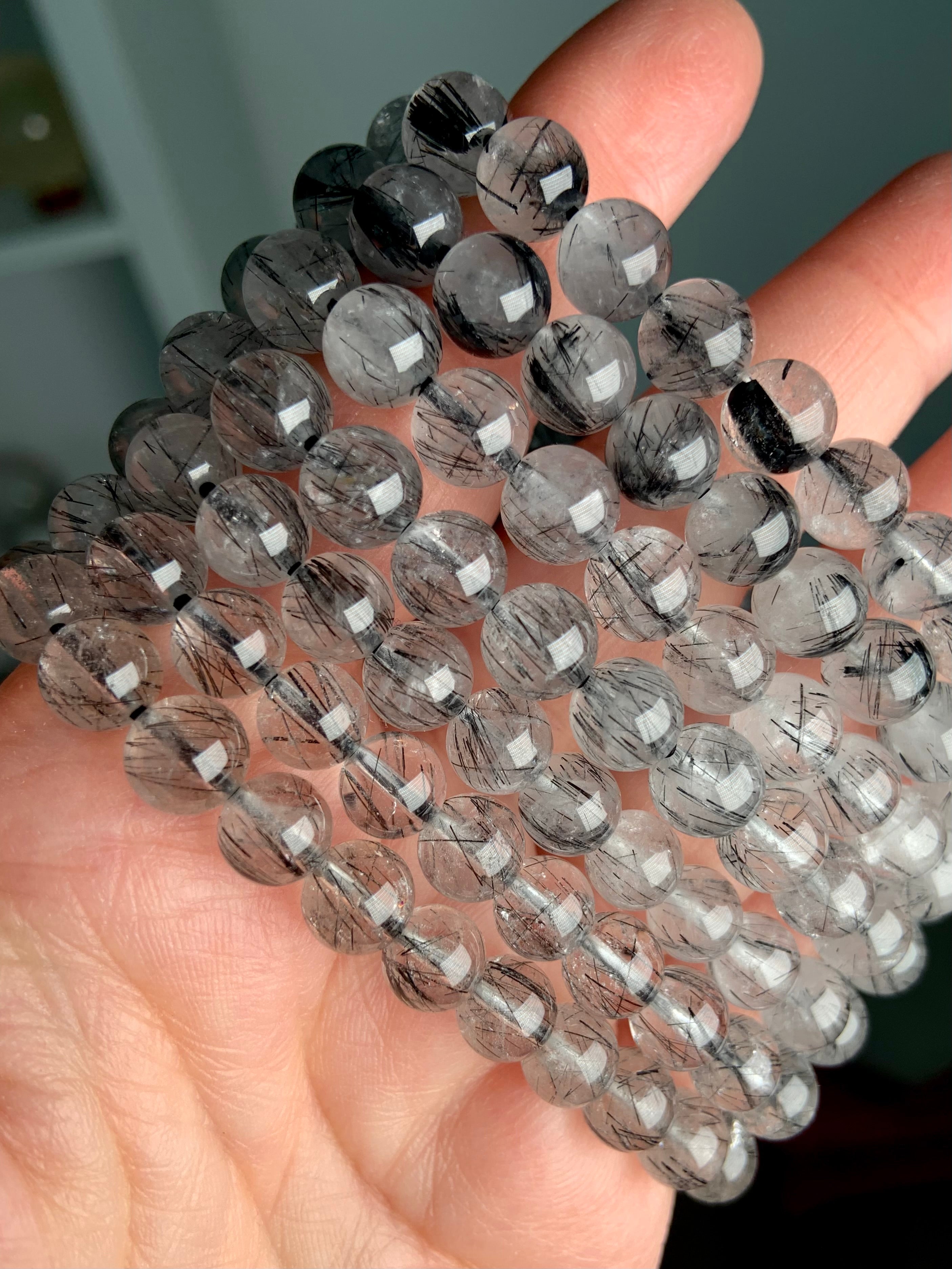 Stack of polished Tourmalinated Quartz bracelets in 7–8mm and 8–9mm beads, showing size variation and striking black rutile inclusions in clear quartz