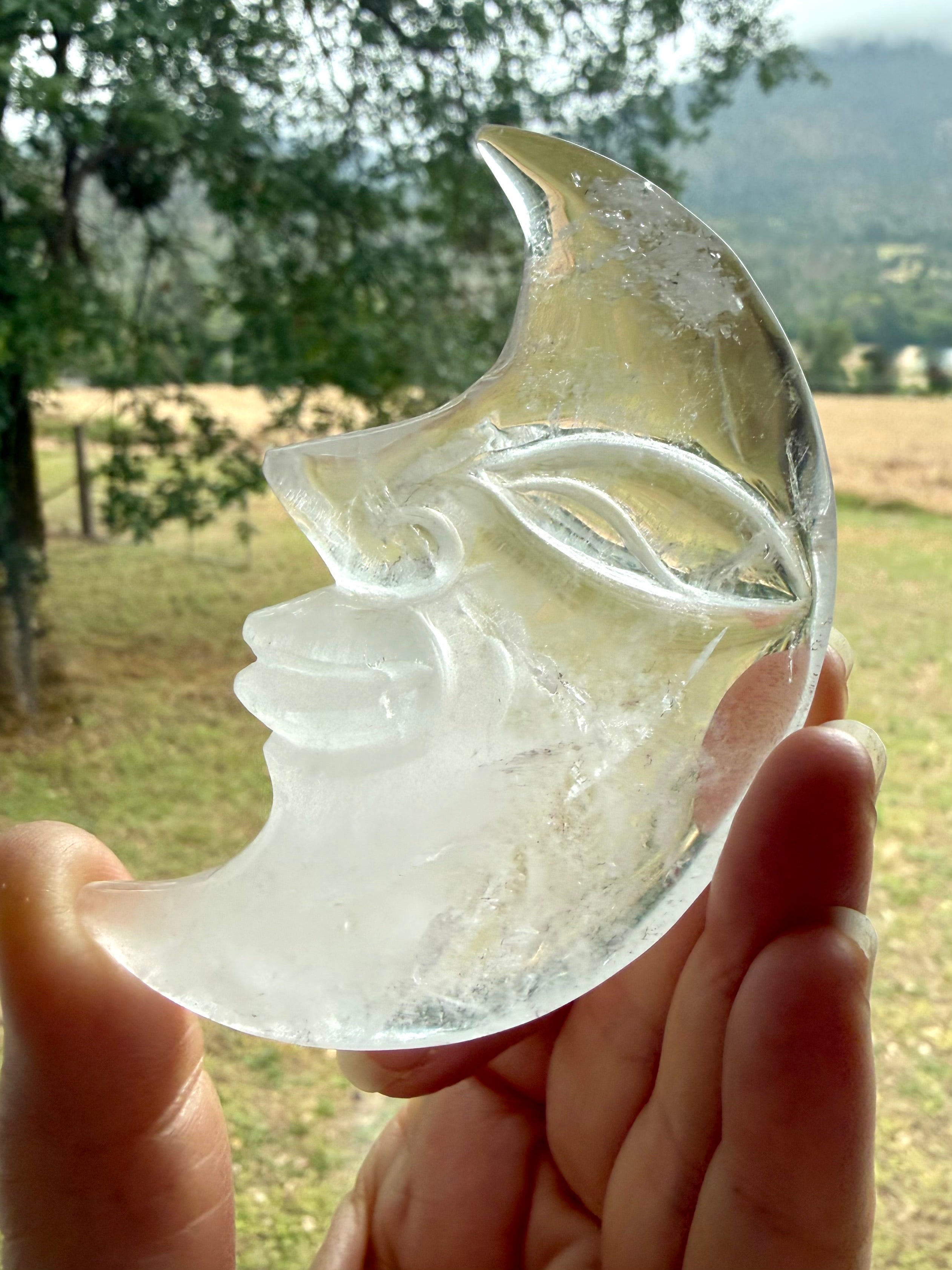 One-of-a-kind Clear Quartz Moon Face carving with a landscape in the background, highlighting clarity, internal patterns, and polished crystal beauty