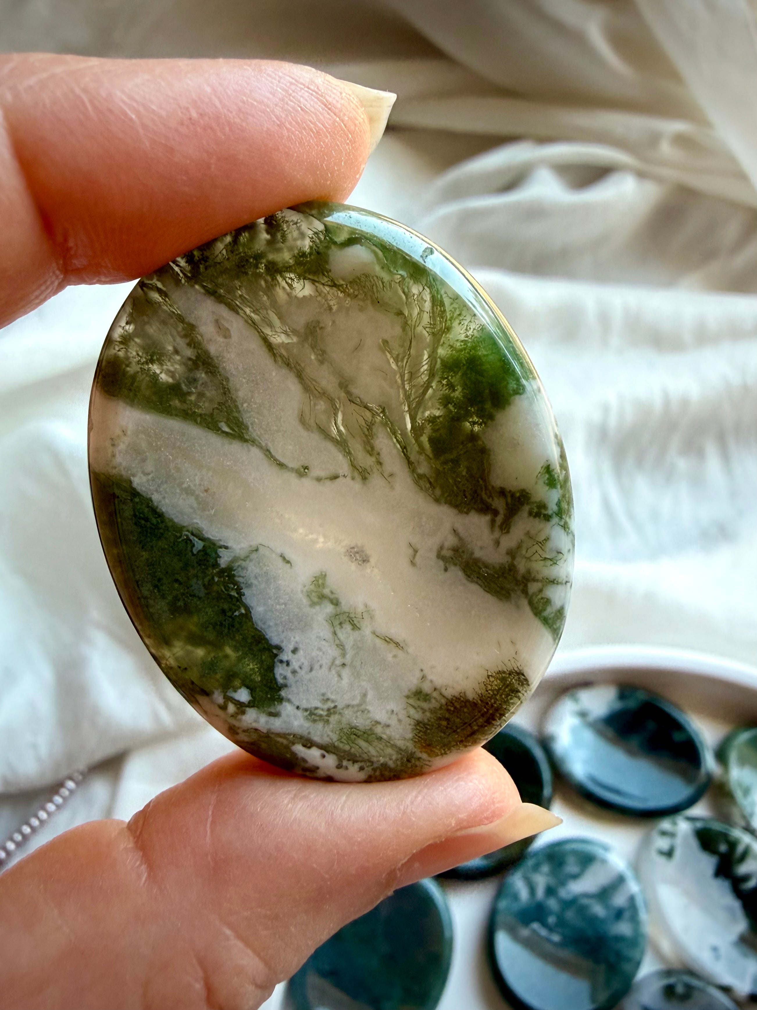 Large Moss Agate oval worry stone held in hand with clear quartz windows and green landscape patterns