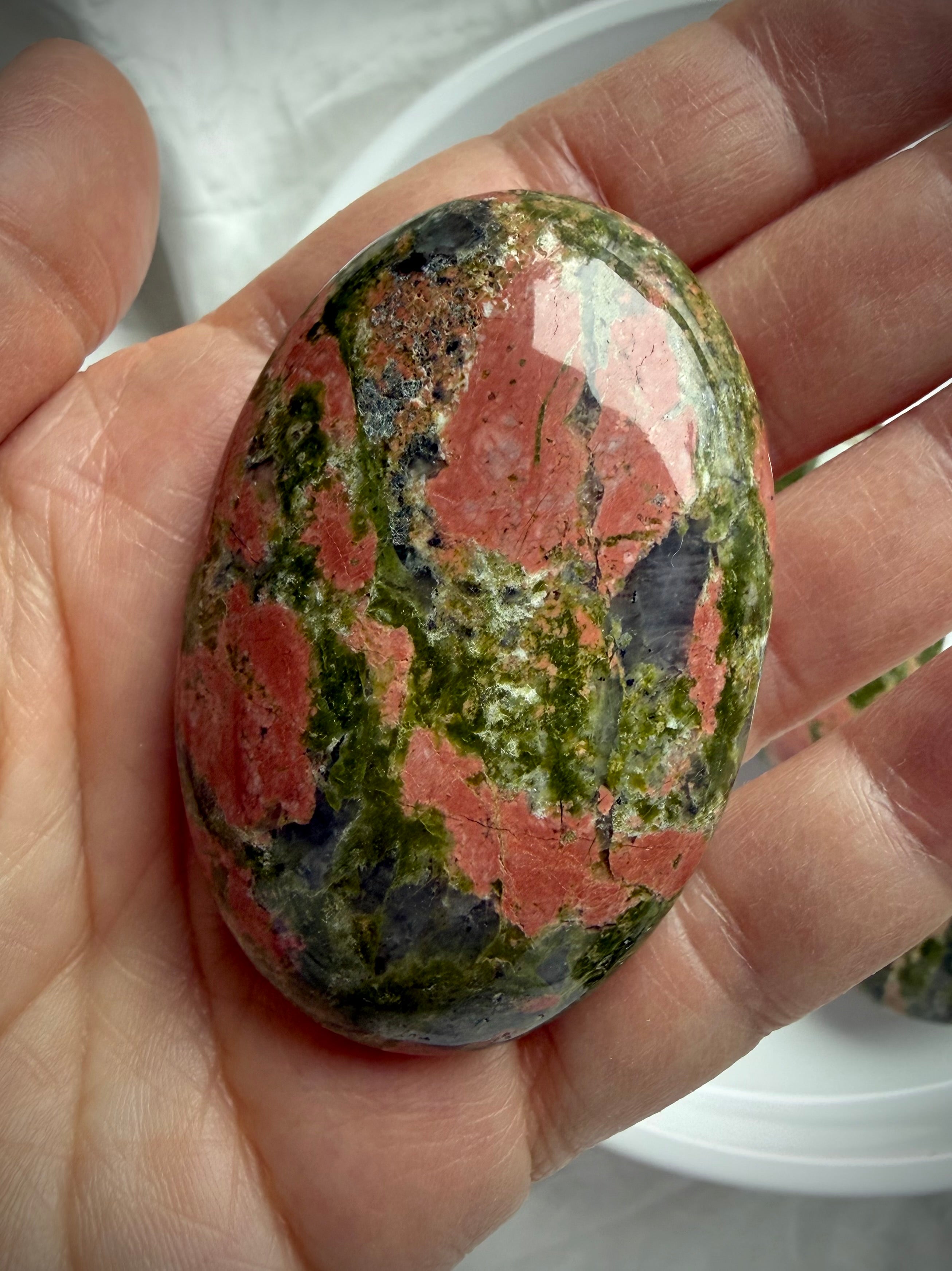 close up Unakite crystal palm stone with mottled green and soft pink mineral patterns for heart healing