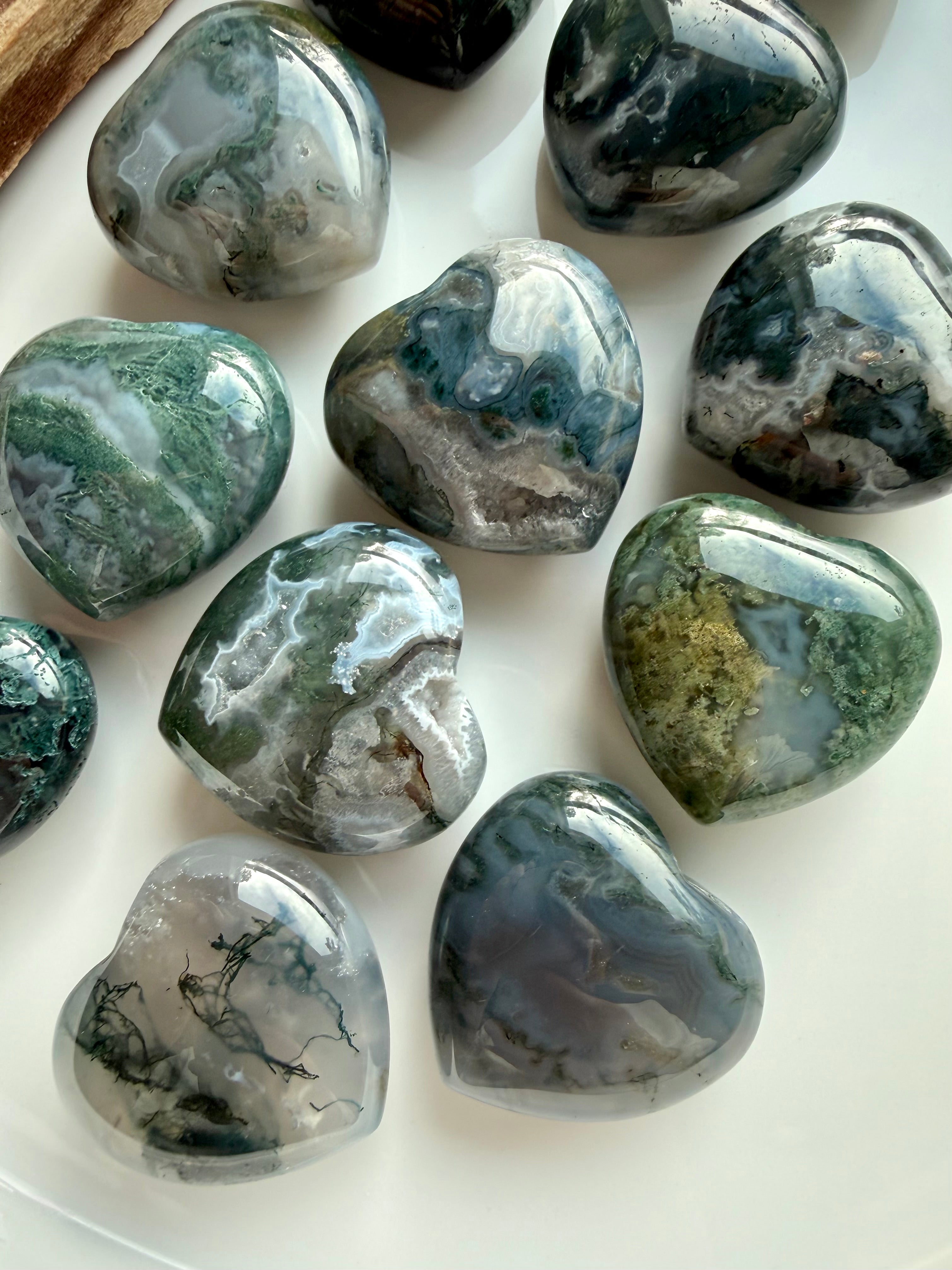 Natural Moss Agate heart crystals with swirling green, grey, and white mineral patterns on a white background