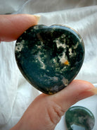 Dark green Moss Agate heart worry stone held in hand with polished natural crystal surface