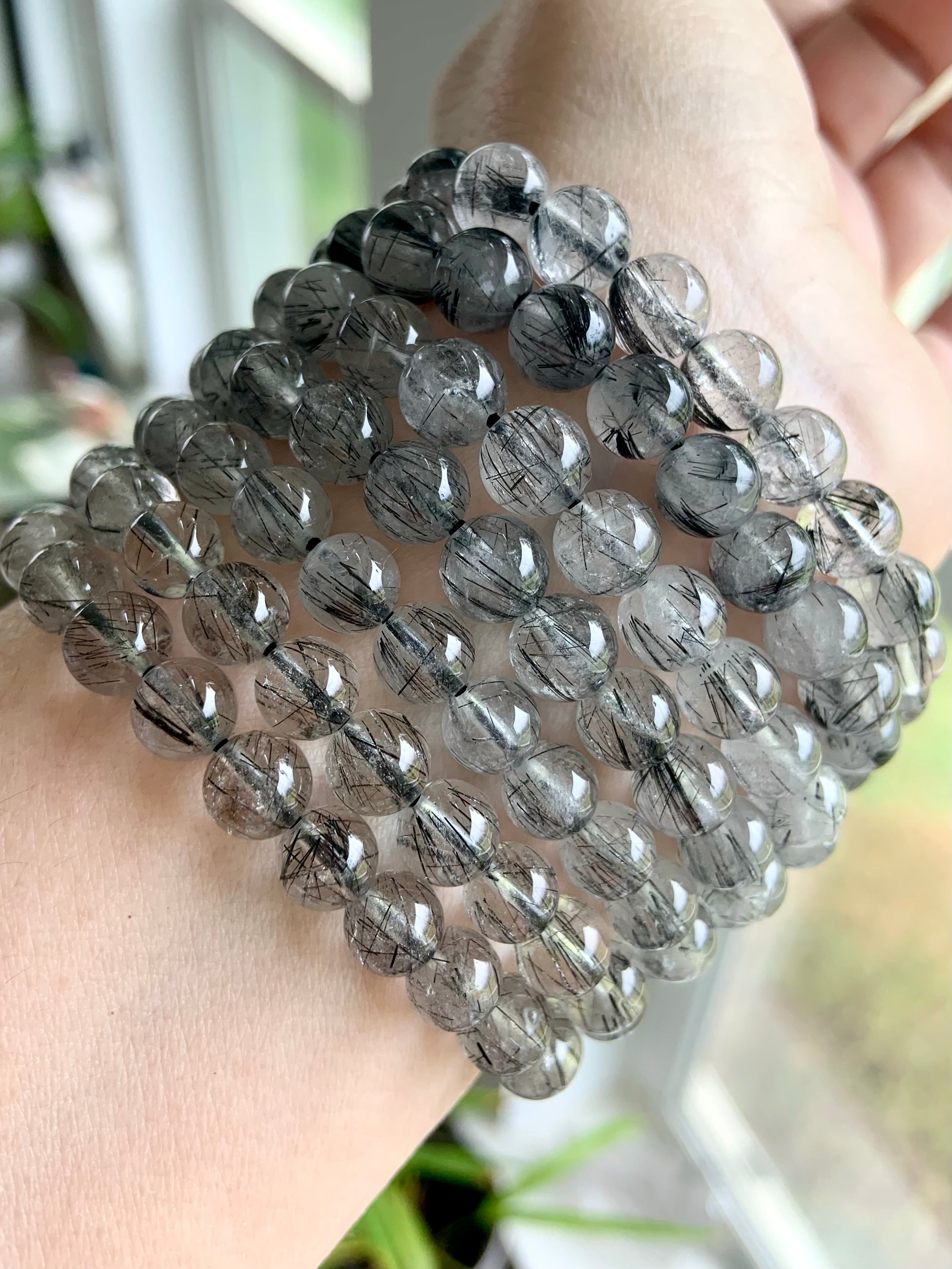 Angled shot of a stack of Tourmalinated Quartz bracelets on a wrist, displaying polished beads and dark rutile strands