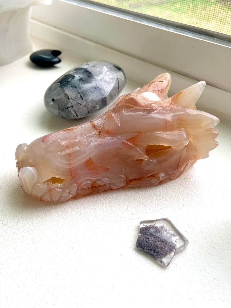 Carnelian Flower Agate Dragon Head Carving photographed in natura light on a windowsill with some other crystals