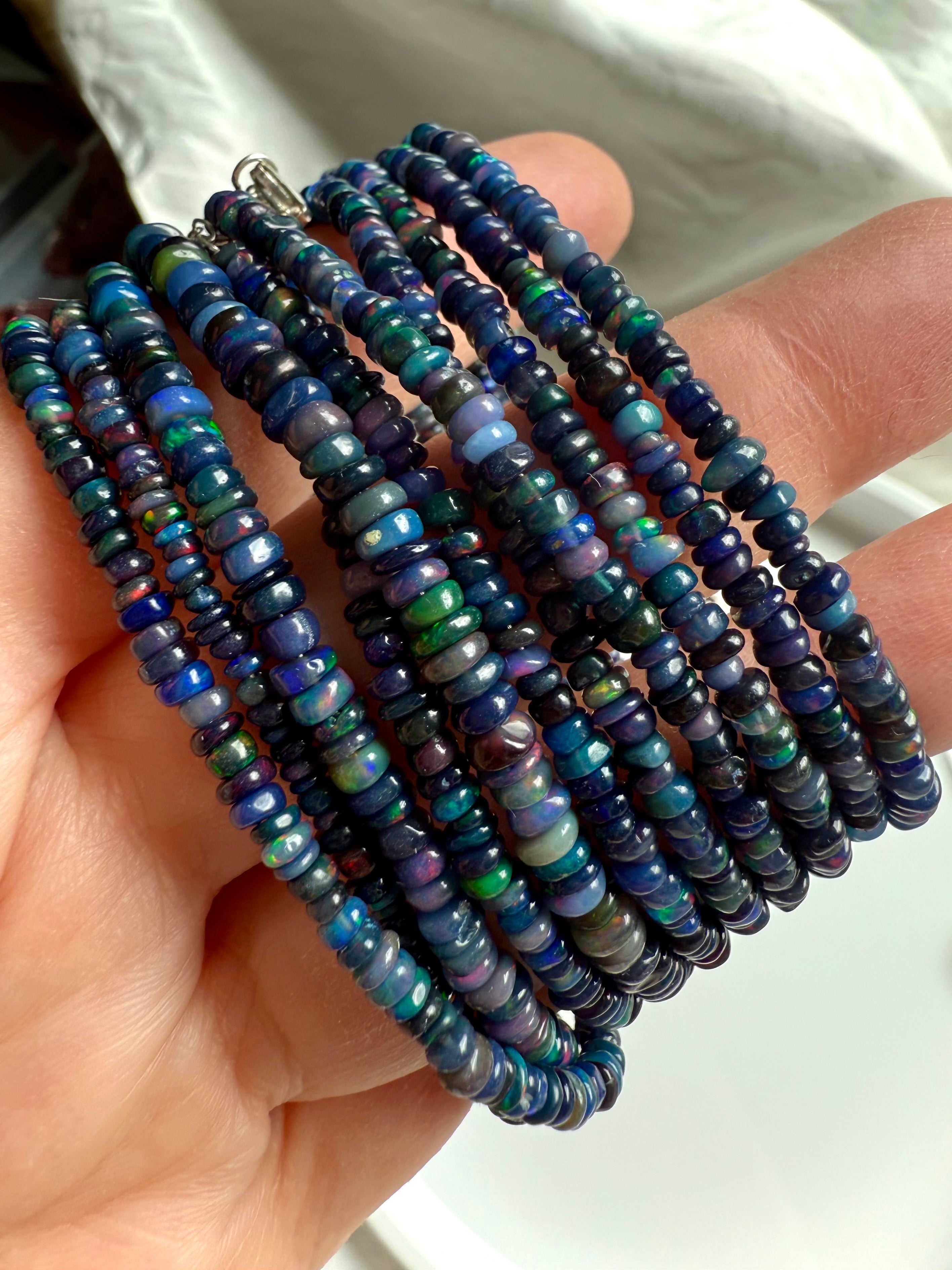 Close-up of multiple Black Fire Opal bracelets in different bead sizes shown at an angle — Ethiopian opal jewelry with fiery blue iridescence.
