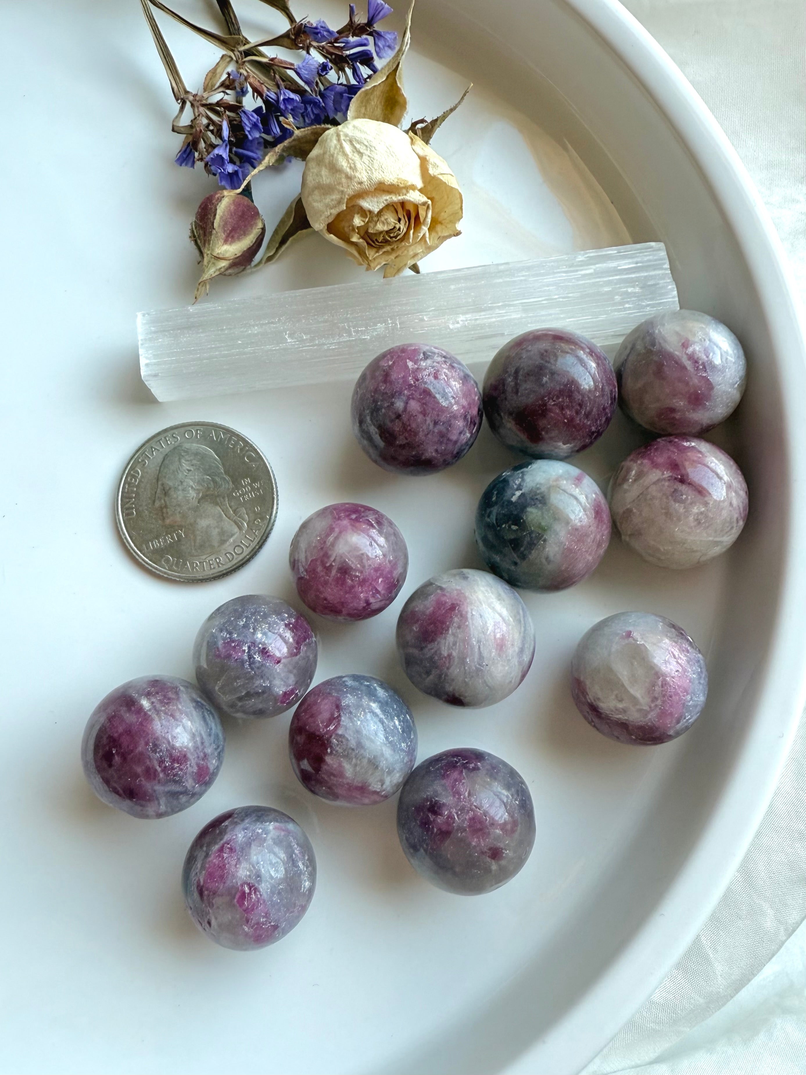 Mini Unicorn Stone spheres with a US quarter for size reference, styled with selenite wand and flowers