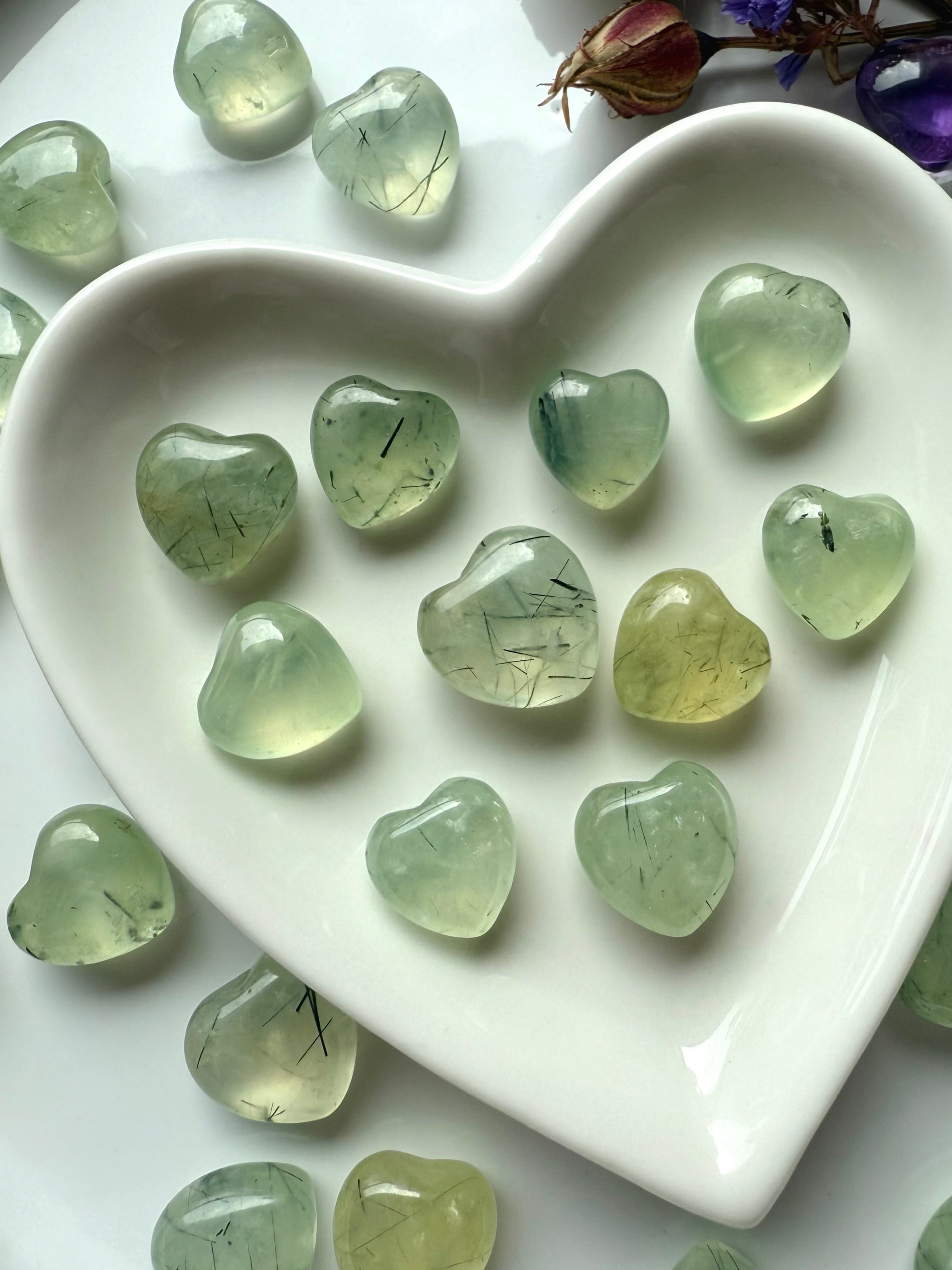 Close up of Prehnite hearts with natural Epidote inclusions in a white heart bowl showing variety in color and crystal patterns.