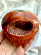 Large Carnelian geode heart held in hand highlighting sparkling druzy crystal cavity and polished natural banding