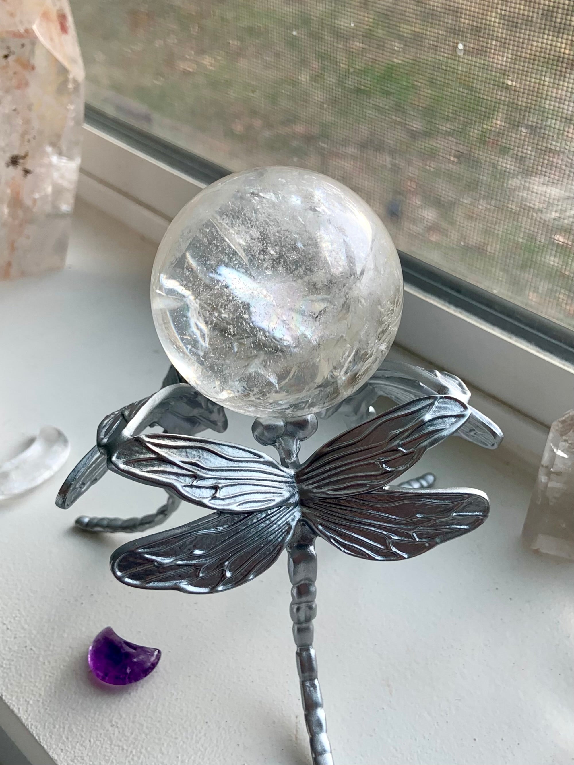 Lifestyle image: silver dragonfly sphere holder with clear quartz crystal ball sitting on a windowsill.
