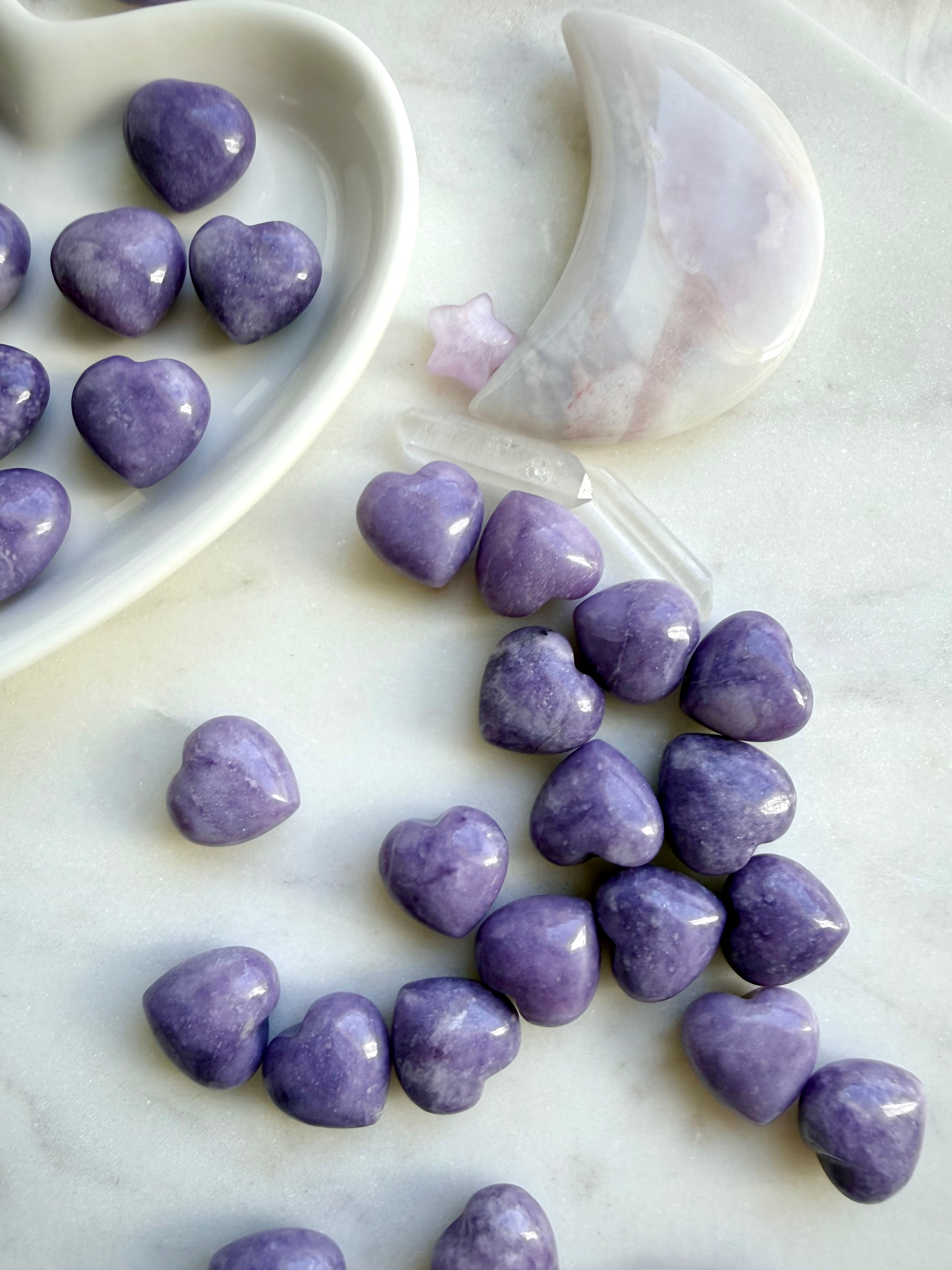 Mini purple Lepidolite heart crystals scattered on a marble background with other crystals