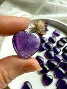 Close-up of an Amethyst crystal heart held gently between fingers, highlighting its violet translucence — a soothing crown chakra stone for inner wisdom and divine guidance.