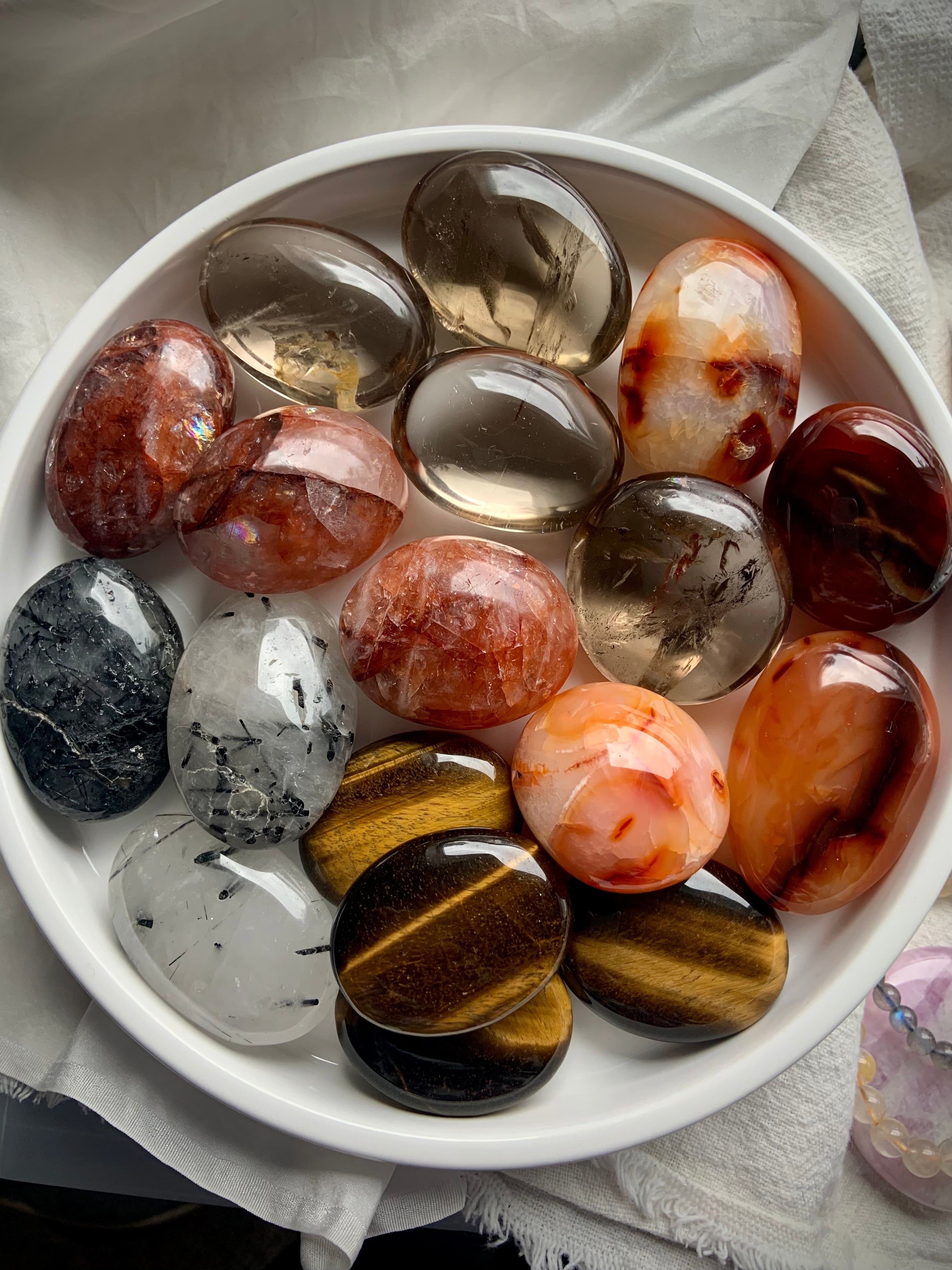 Overhead view of chakra crystal palm stones on a white plate — shows size, shape &amp; color variety in this grounding crystal set.