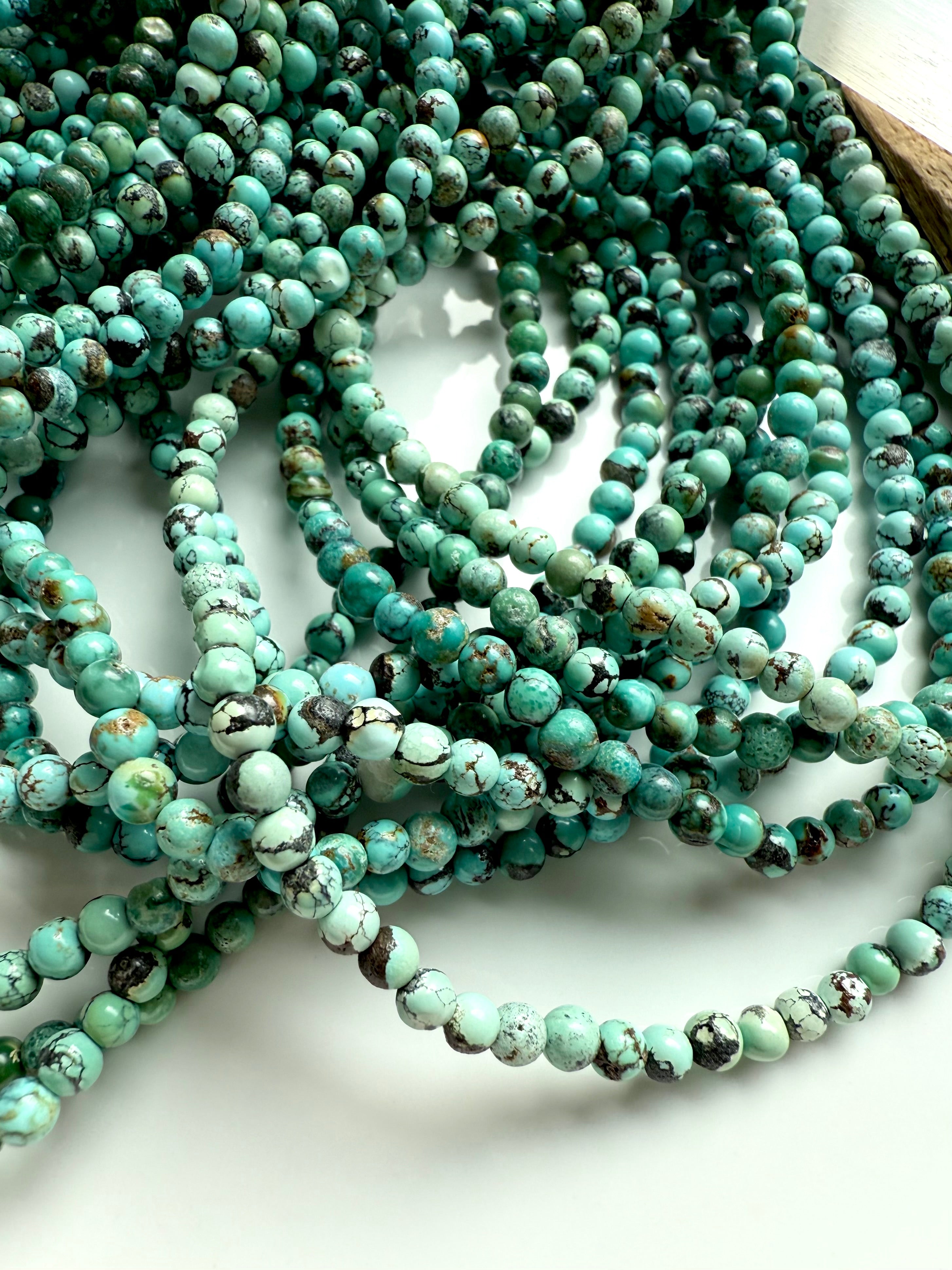 Tumbled pile of turquoise 4mm bead strands in shades of teal, mint, and aqua green