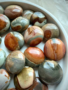 Small Desert Jasper palm stones with contrasting green, rust red, cream, and tan patterns displayed in a white ceramic bowl