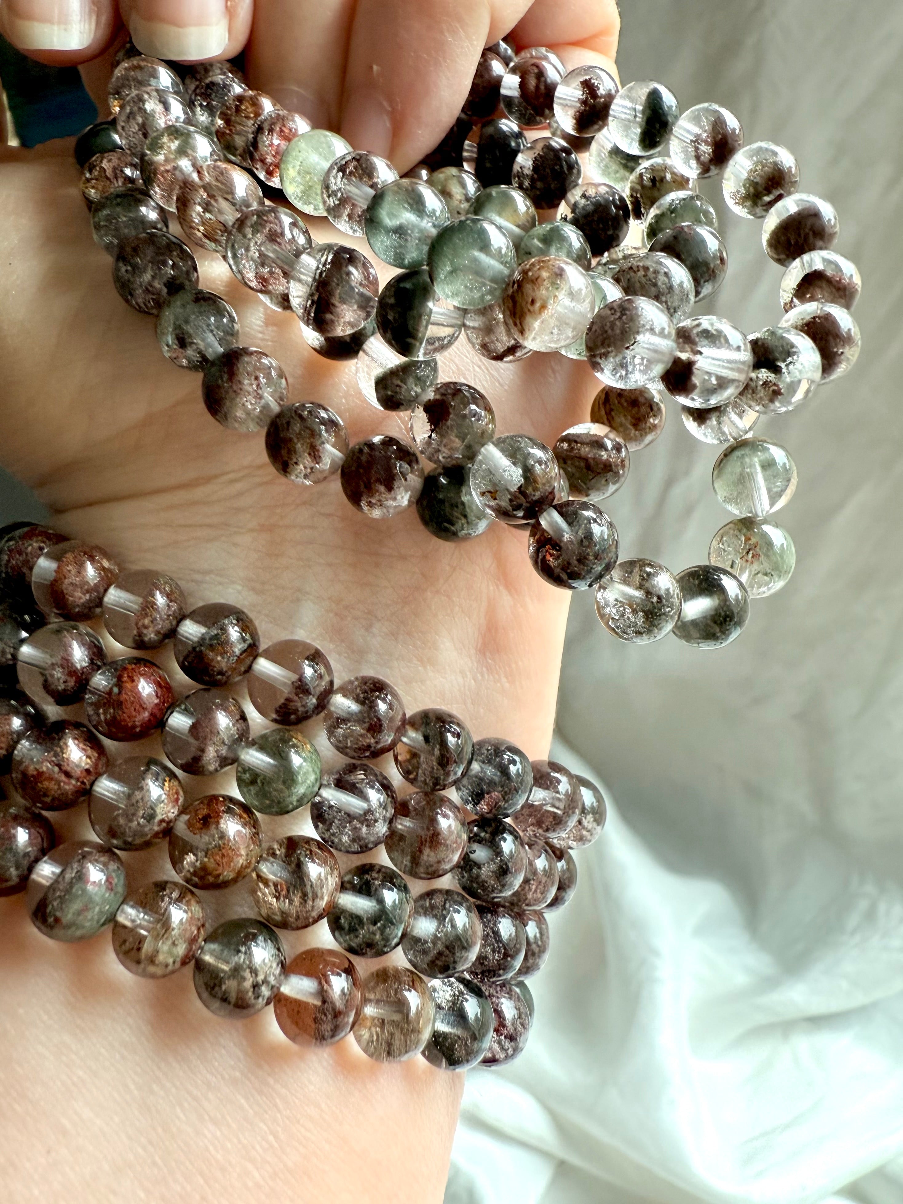 Close-up of Garden Quartz bracelet beads with mossy inclusions and earthy red-brown phantoms, hand model in soft light 