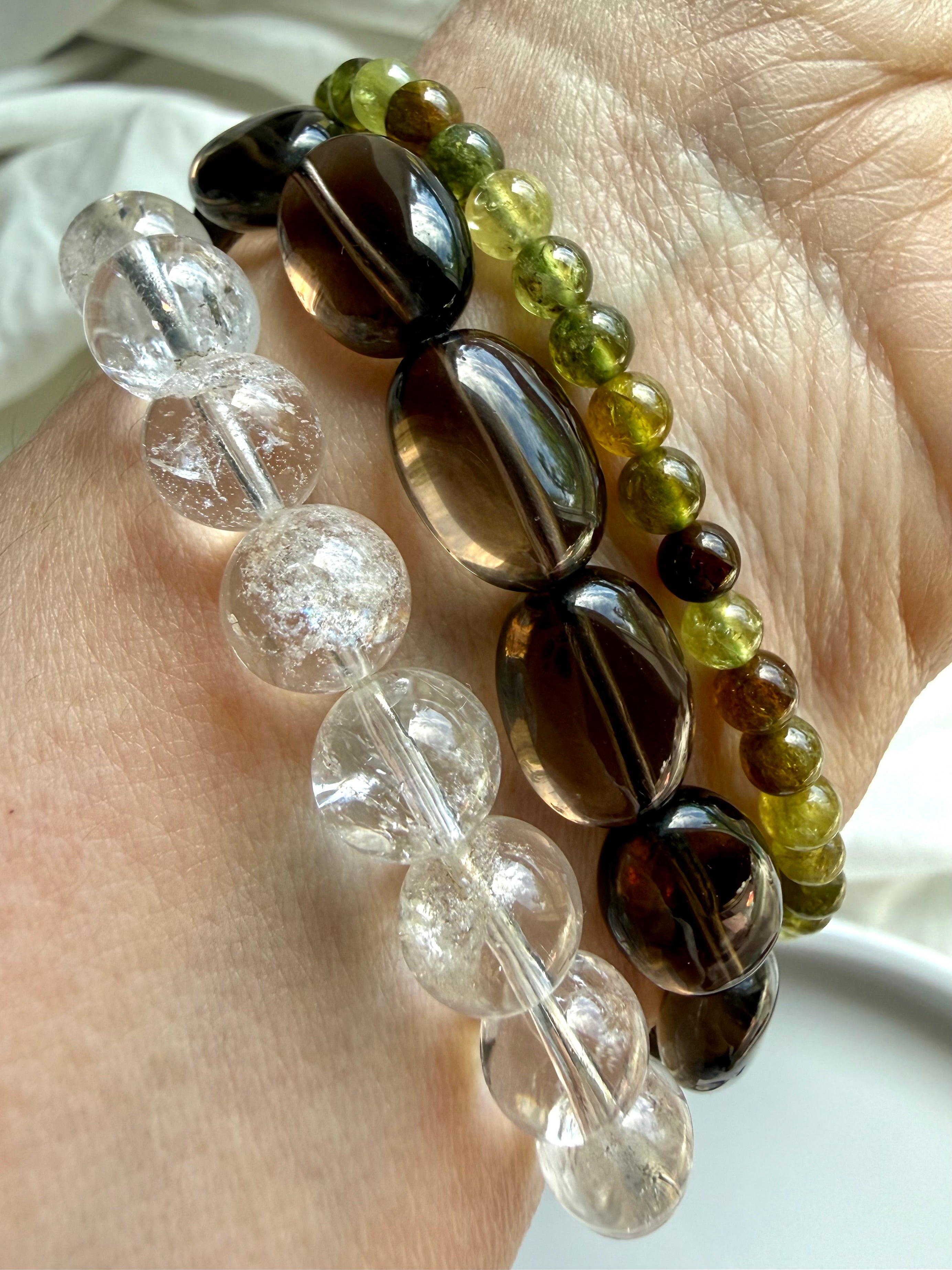 Rainbow Quartz, Smoky Quartz, and Tsavorite Garnet bracelet stack with transparent crystal gemstones and earthy neutral tones