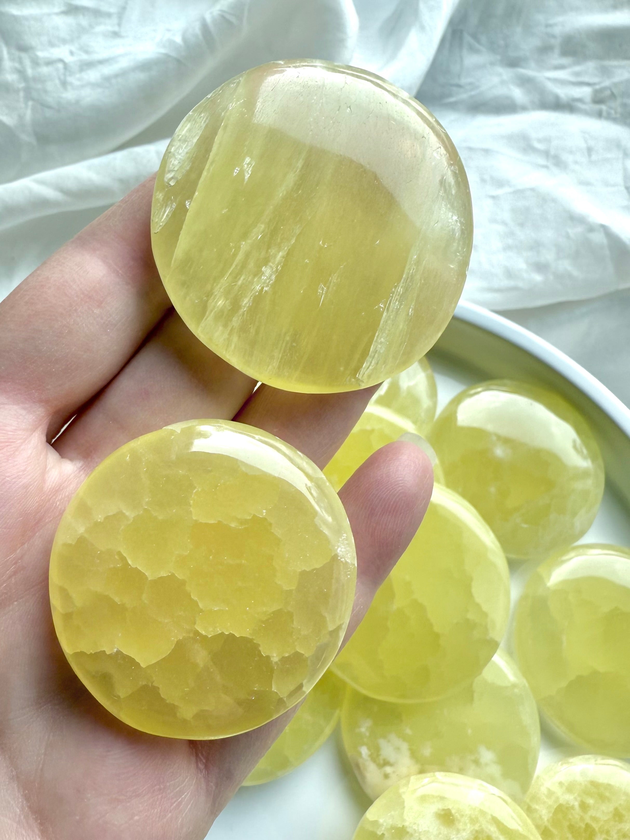 Hand holding two lemon calcite crystal discs showing smooth polish, natural texture, and vibrant color