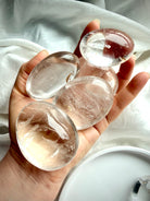five clear quartz palm stones held in hand showing high clarity, natural inclusions, and polished finish