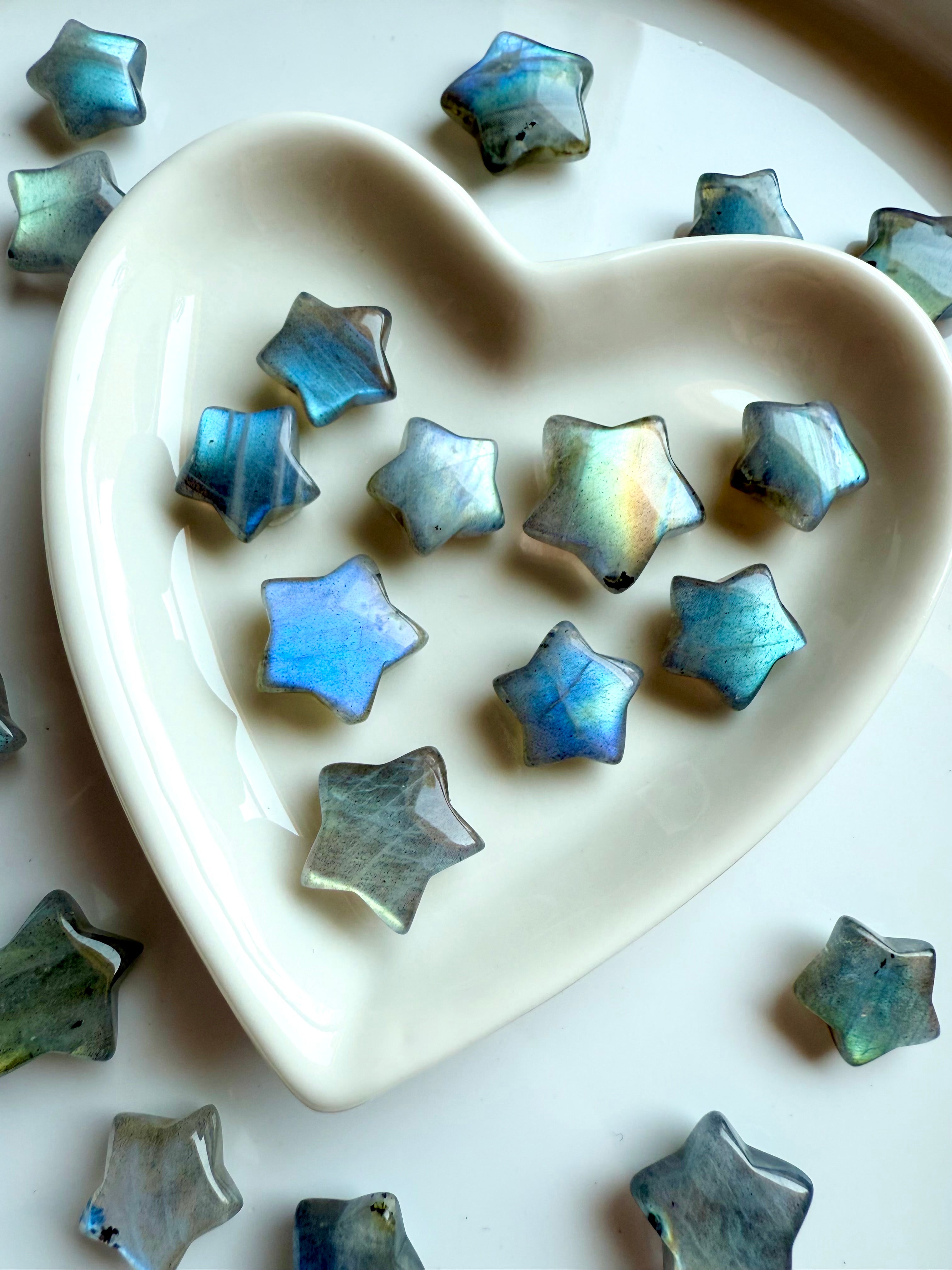 Close-up of pastel Labradorite crystal stars inside a white ceramic heart bowl — soft shimmer mini star carvings for peace, intuition &amp; gentle protection.