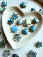 Close-up of pastel Labradorite crystal stars inside a white ceramic heart bowl — soft shimmer mini star carvings for peace, intuition & gentle protection.