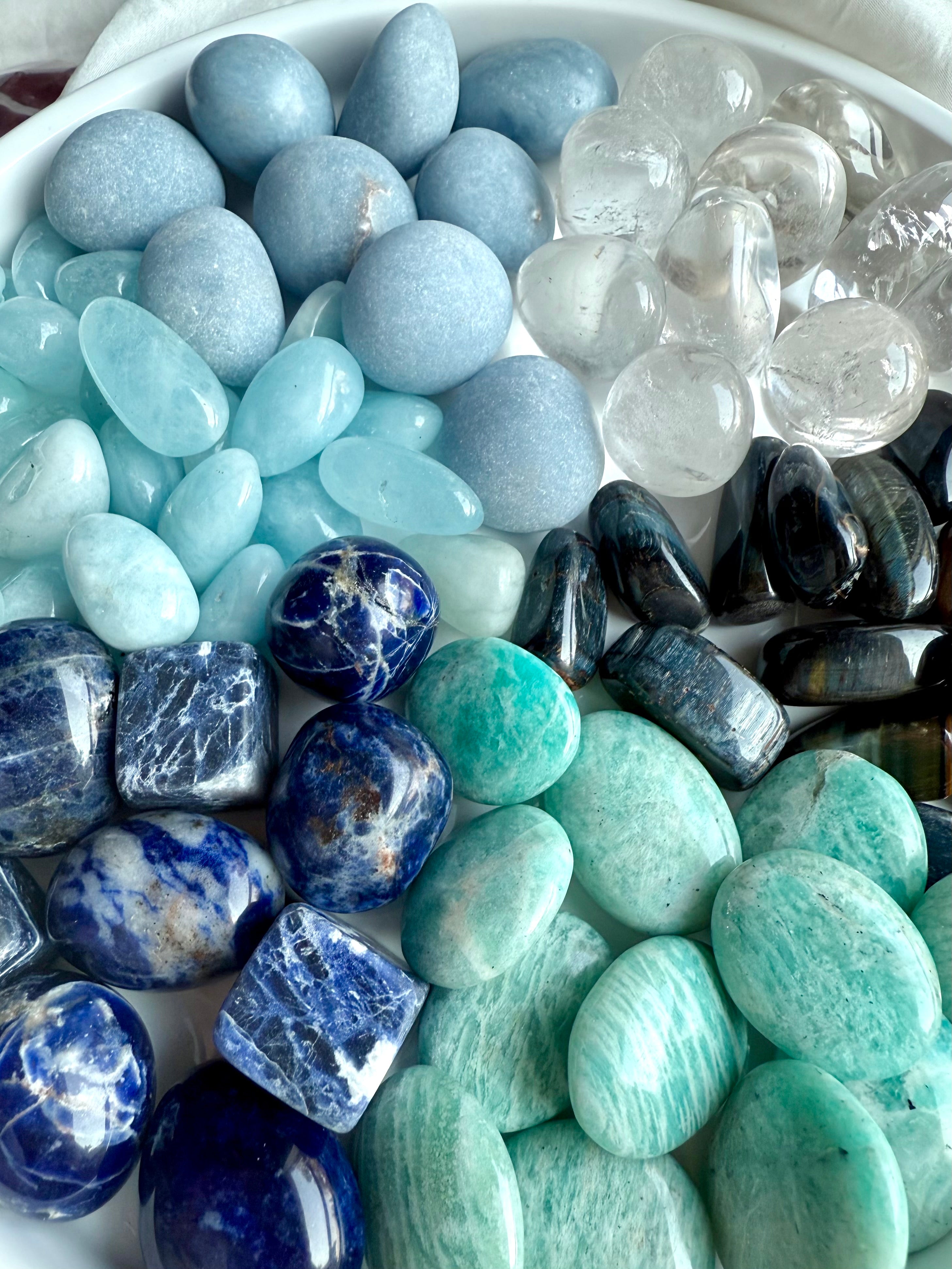 Close-up of Throat Chakra Crystal Set — Angelite, Sodalite, Amazonite, Aquamarine, Blue Tiger’s Eye, and Clear Quartz healing stones on white plate.