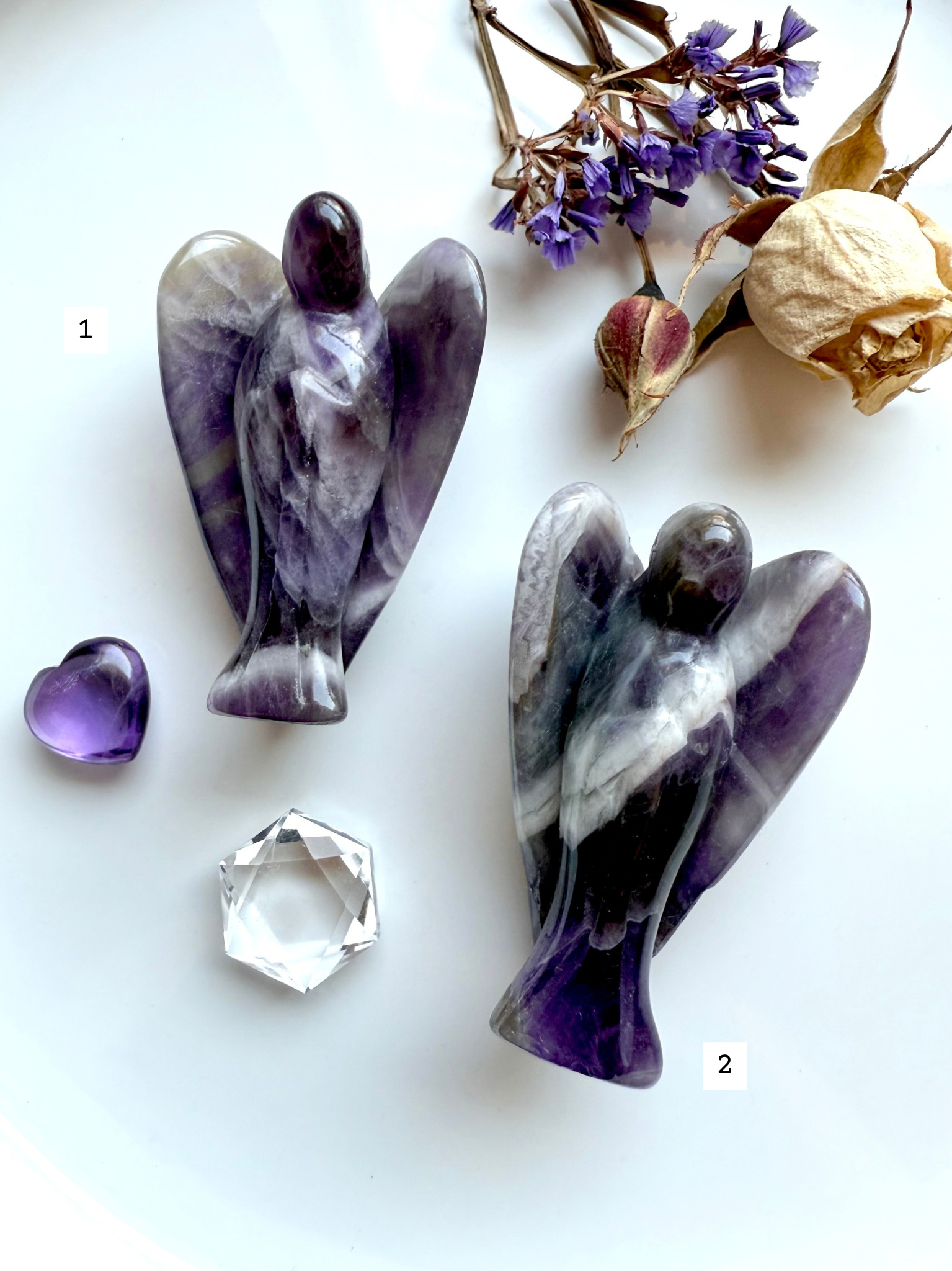 Choose-your-own Dream Amethyst angel carvings marked as #1 and #2, shown with dried flowers, purple Amethyst heart, and faceted quartz – ethically sourced from Zambia for peace and clarity