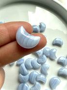 Small polished Blue Lace Agate crescent moon carving held between fingers to show detailed banding and size