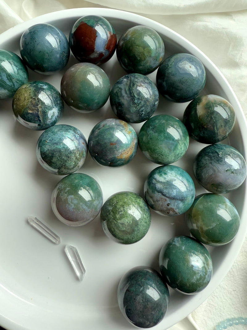 Colorful moss agate mini spheres shown on a white plate with some other crystals