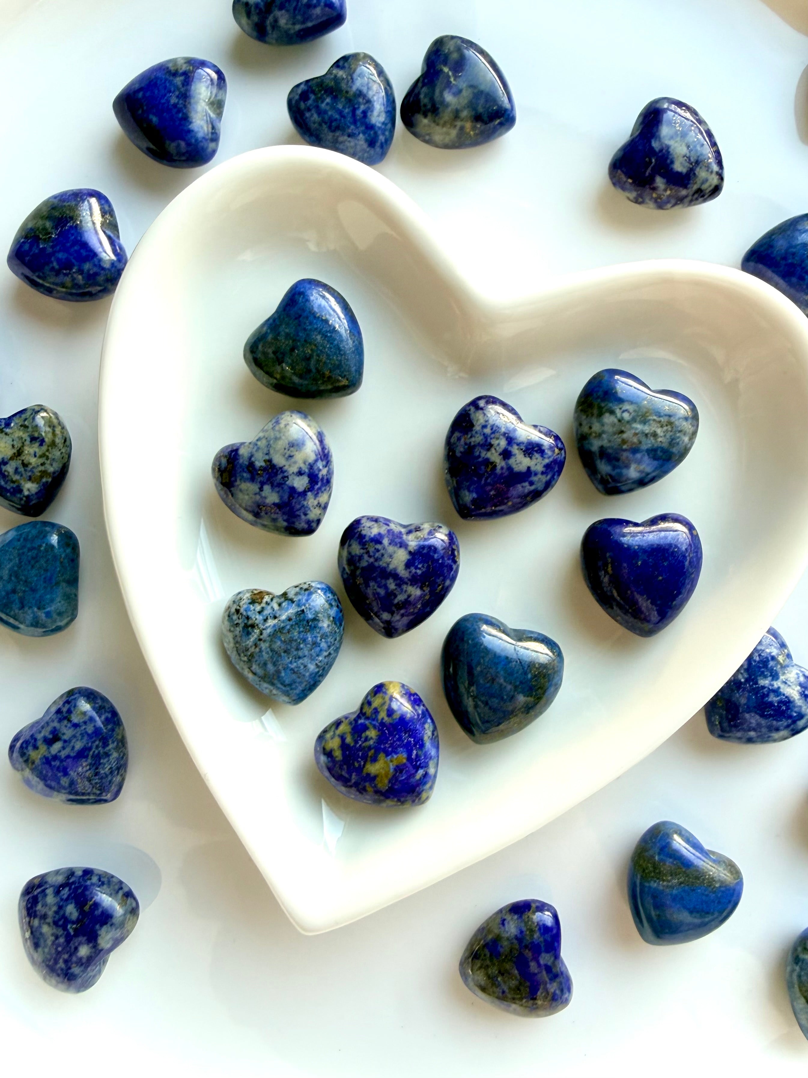 Assorted Mini Lapis Lazuli heart carvings displayed in a white heart dish, polished blue crystal hearts with natural pattern variation, each stone unique