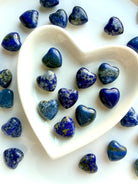 Assorted Mini Lapis Lazuli heart carvings displayed in a white heart dish, polished blue crystal hearts with natural pattern variation, each stone unique