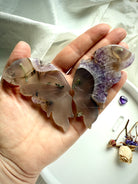 Hand holding carved agate butterfly wings with amethyst druzy edges, showing translucent banding and natural inclusions.