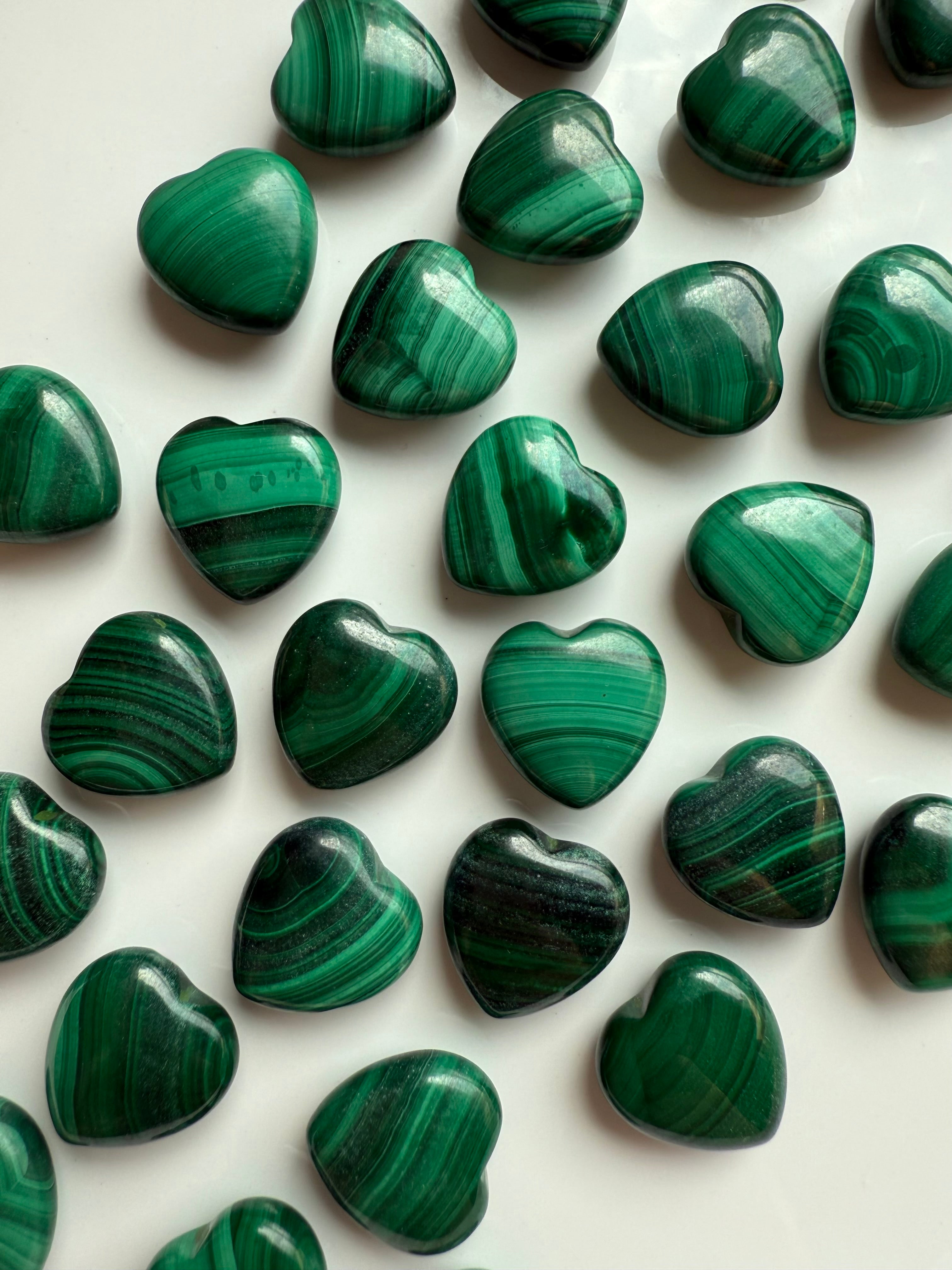 Close-up of polished Malachite heart carvings showing rich banded patterns in vibrant green tones.