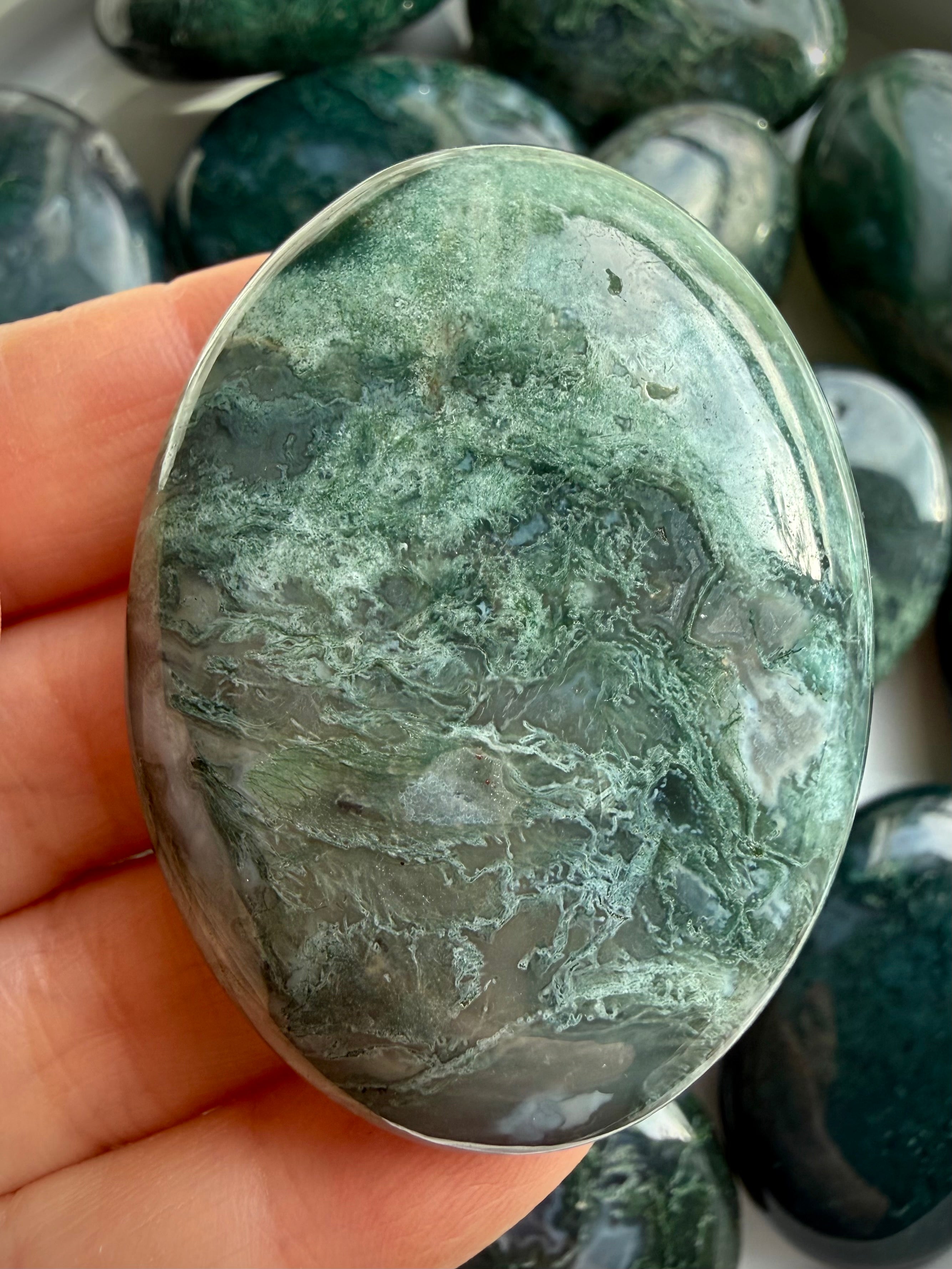 Close-up moss agate palm stone with translucent chalcedony and moss-like inclusions, soothing grounding crystal