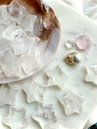 Closeup of Clear Quartz stars spilling out of a seashell onto granite surface with other celestial crystals, luminous chakra healing carvings