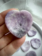 Lepidolite heart worry stone in hand showing mottled lilac purple color with white, black and gray inclusions