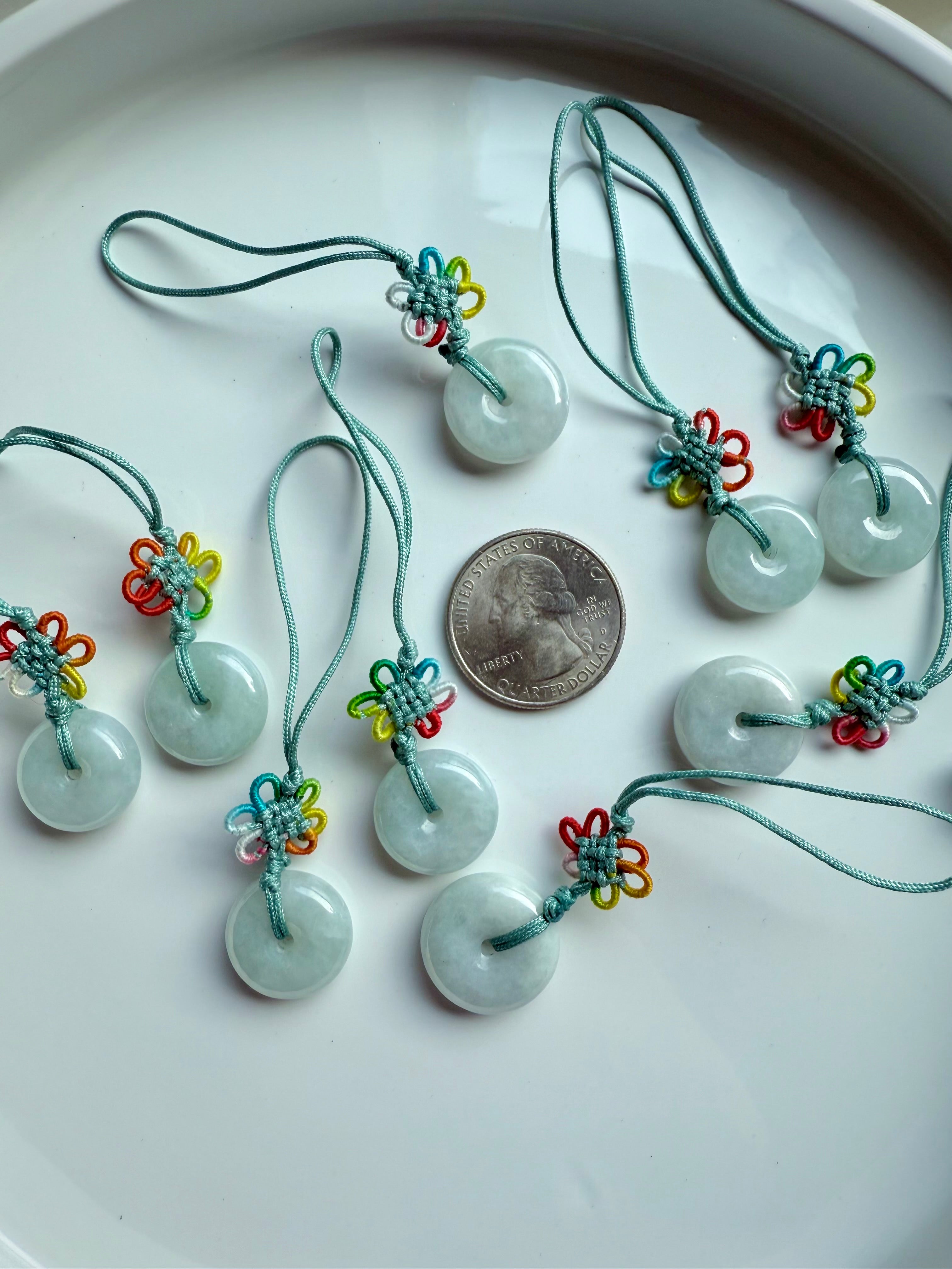 Jade donut charms with colorful knots arranged in a group beside a US quarter for size reference