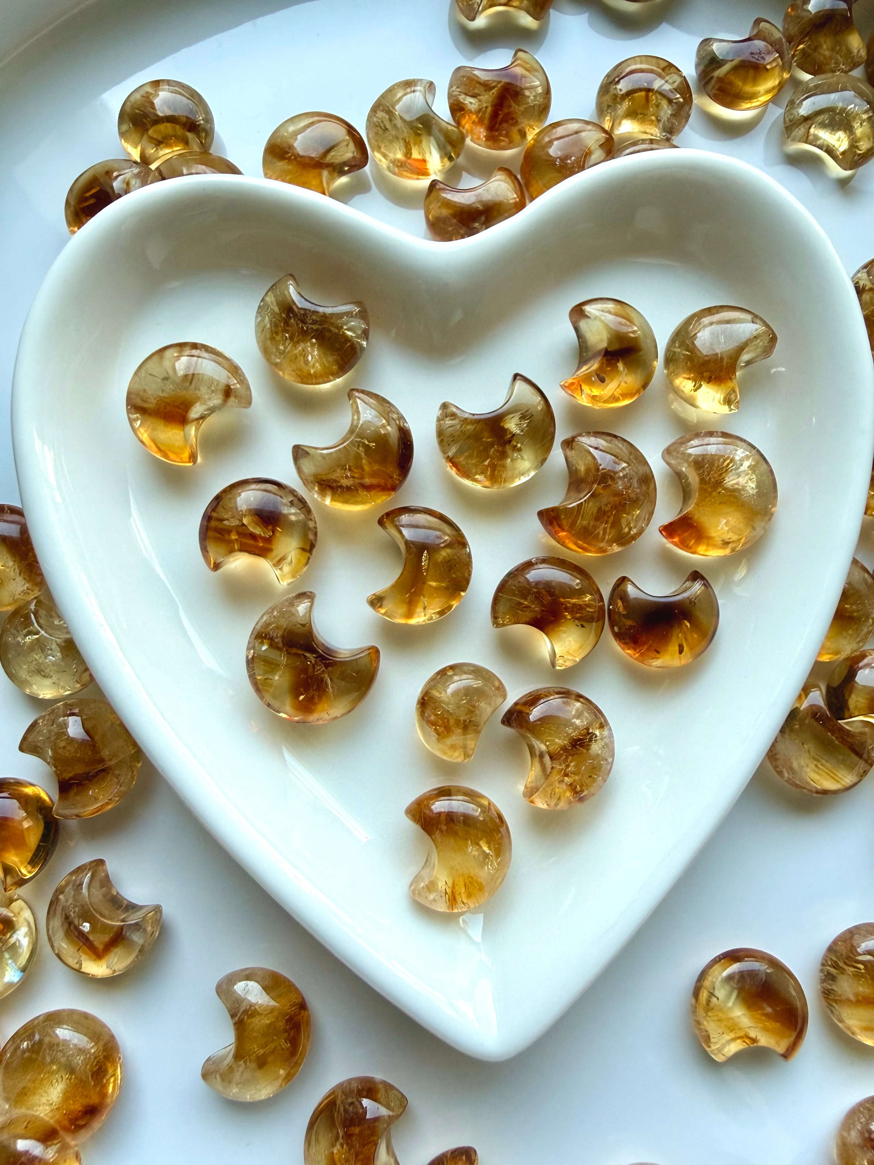 Mini Citrine moons in luminous golden honey and amber tones displayed in a white heart-shaped crystal dish