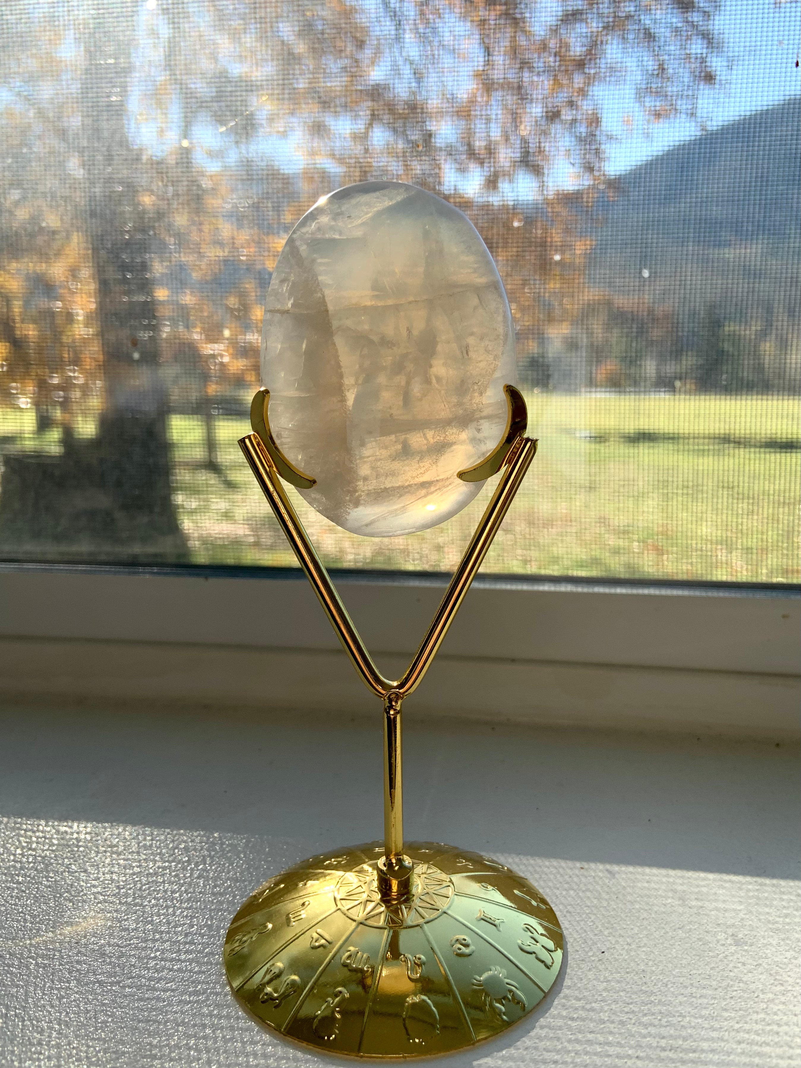 Gold crystal stand displaying a translucent Girasol Quartz palm stone — ideal crystal holder to let light shine through your healing stones