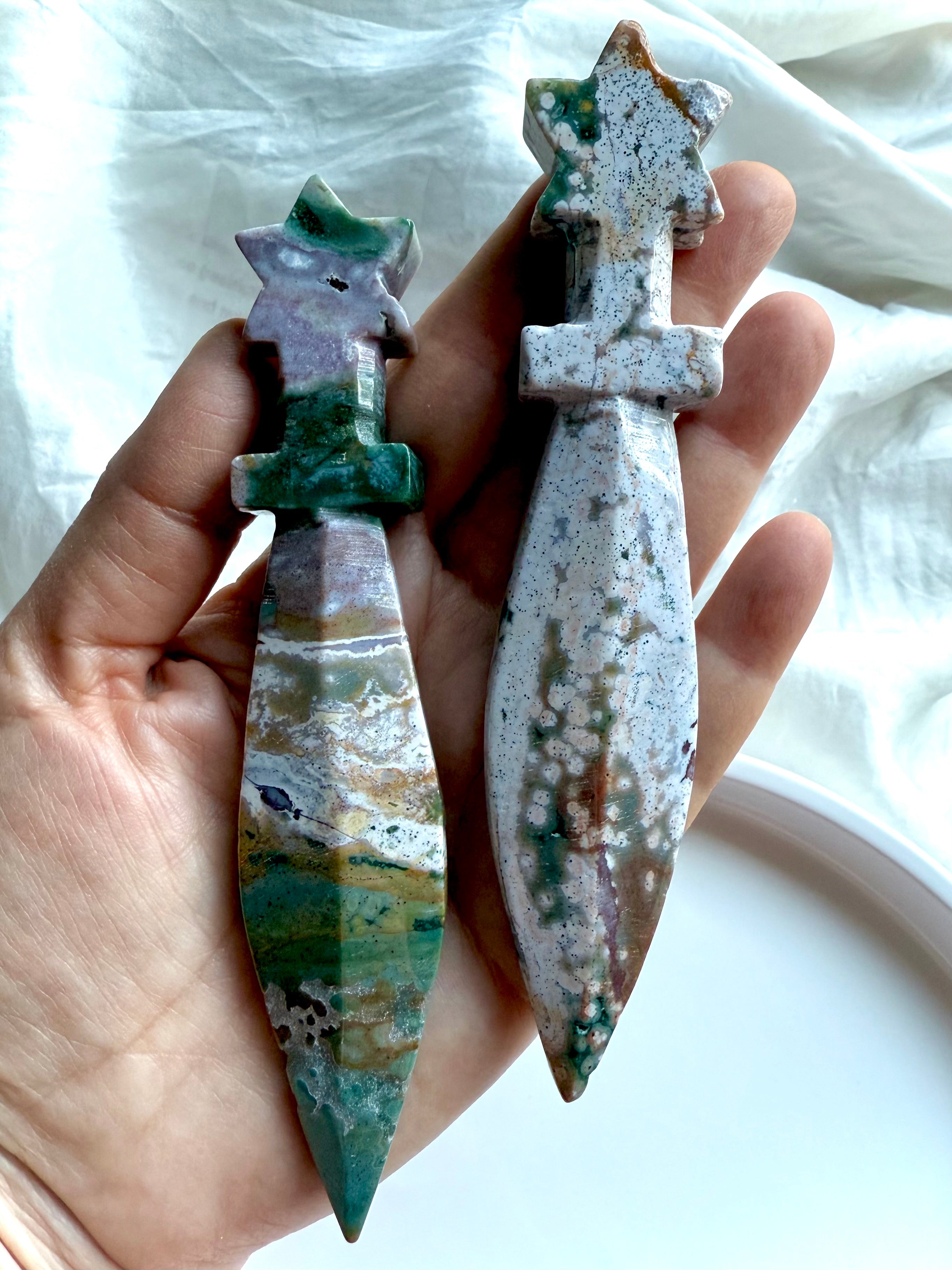 Two Ocean Jasper star knives with carved star handles and smooth stone blades, held in hand to show size and natural color variations