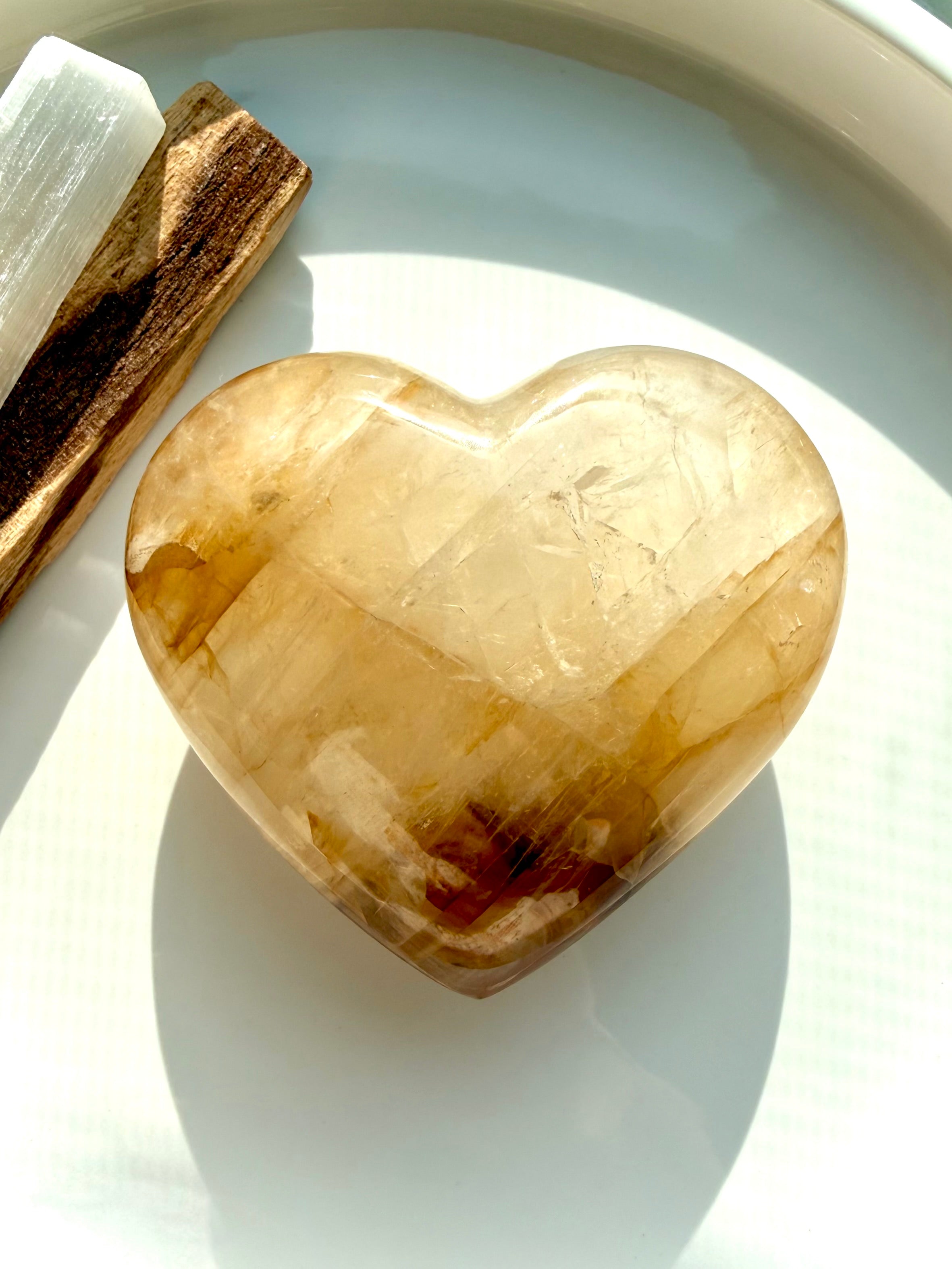 Golden Healer quartz heart styled with palo santo and selenite on white tray for energy clearing and Solar Plexus activation