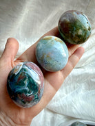 Three Ocean Jasper palm stones held in hand, featuring teal green, blue-gray, and pink mineral patterns