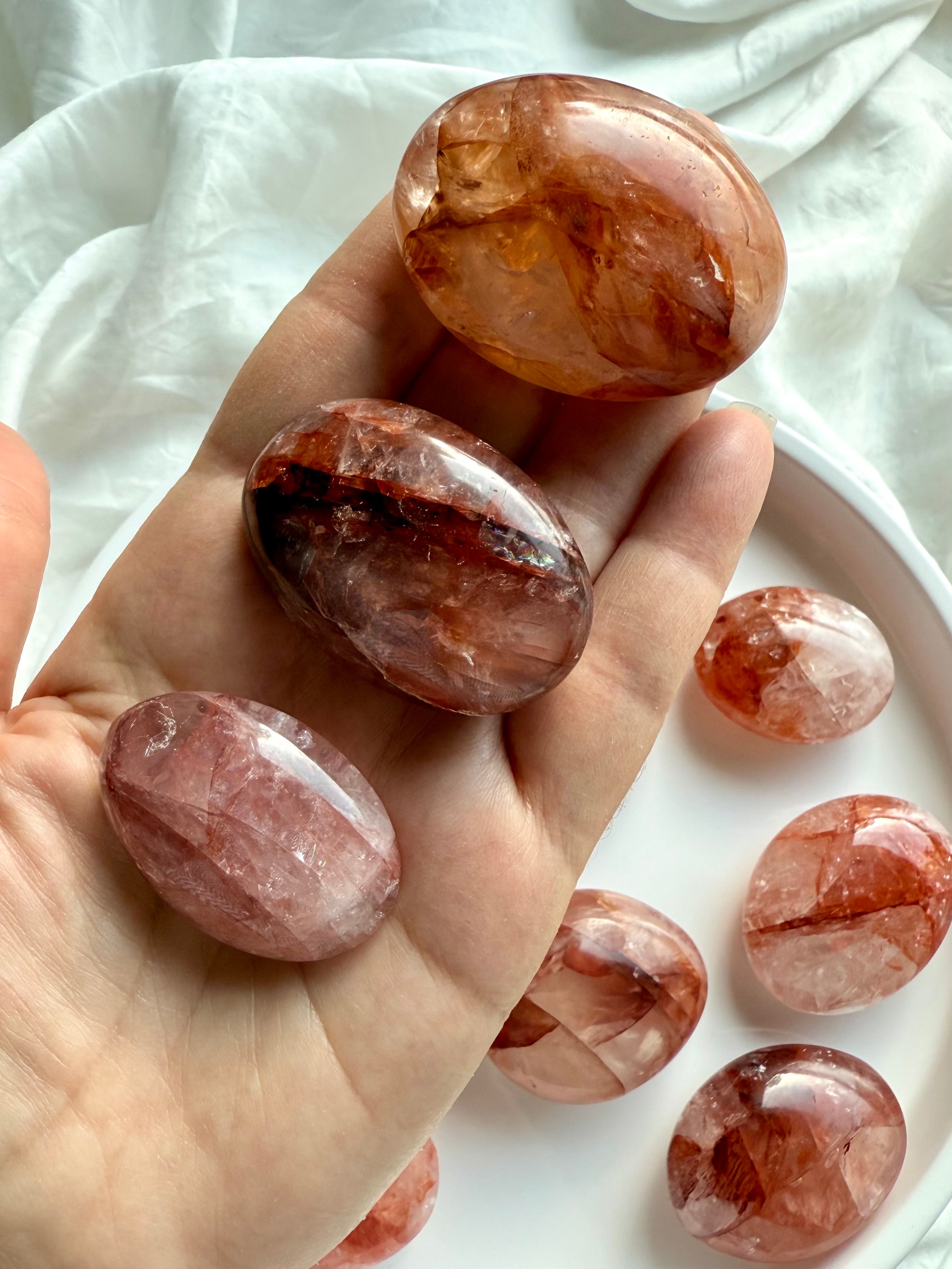 Hand holding polished Hematoid Quartz palm stones in red and orange hues for chakra balancing
