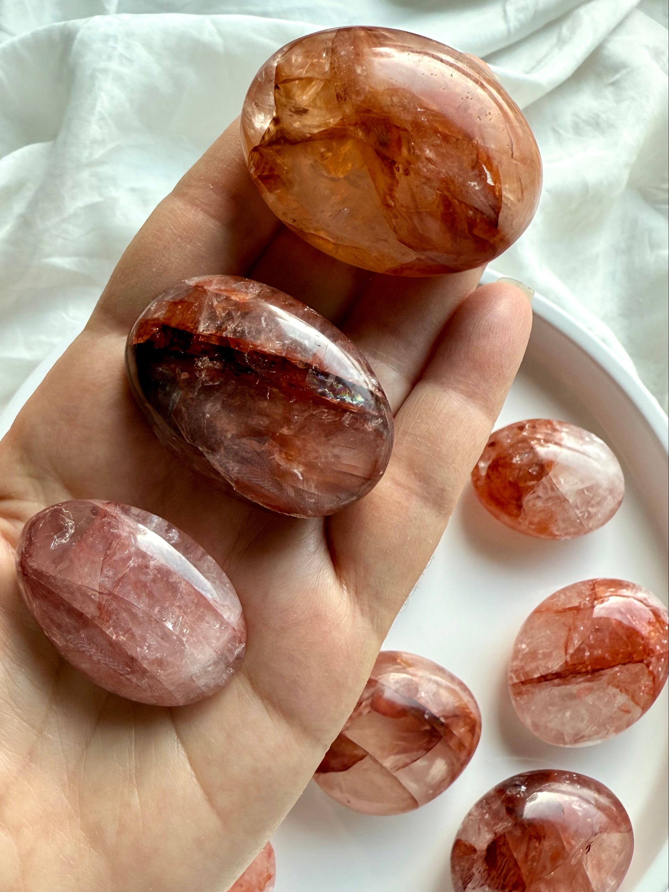 Hand holding polished Hematoid Quartz palm stones in red and orange hues for chakra balancing
