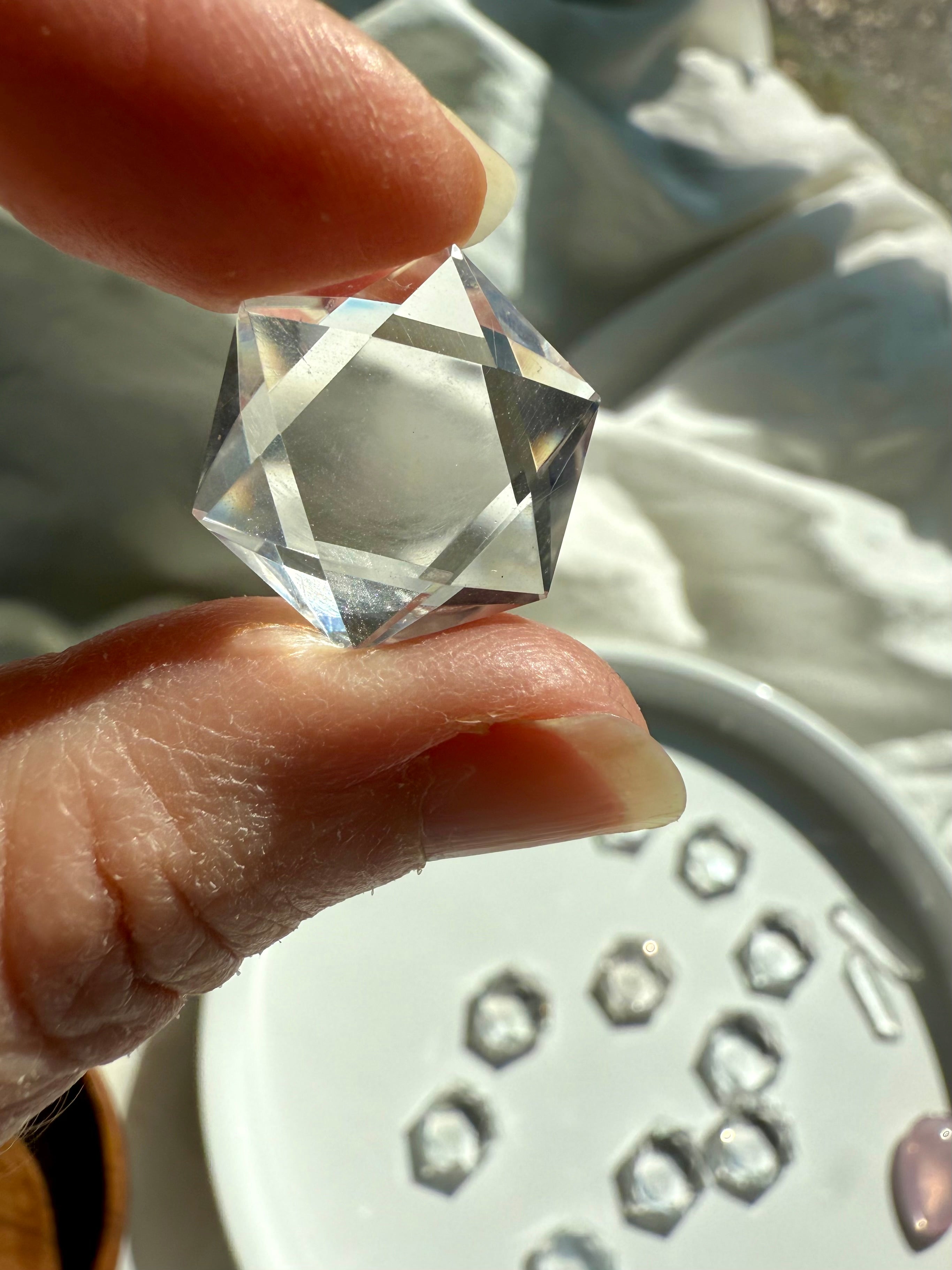 Closeup of Clear Quartz hexagon held to the light with plate of crystals blurred in background