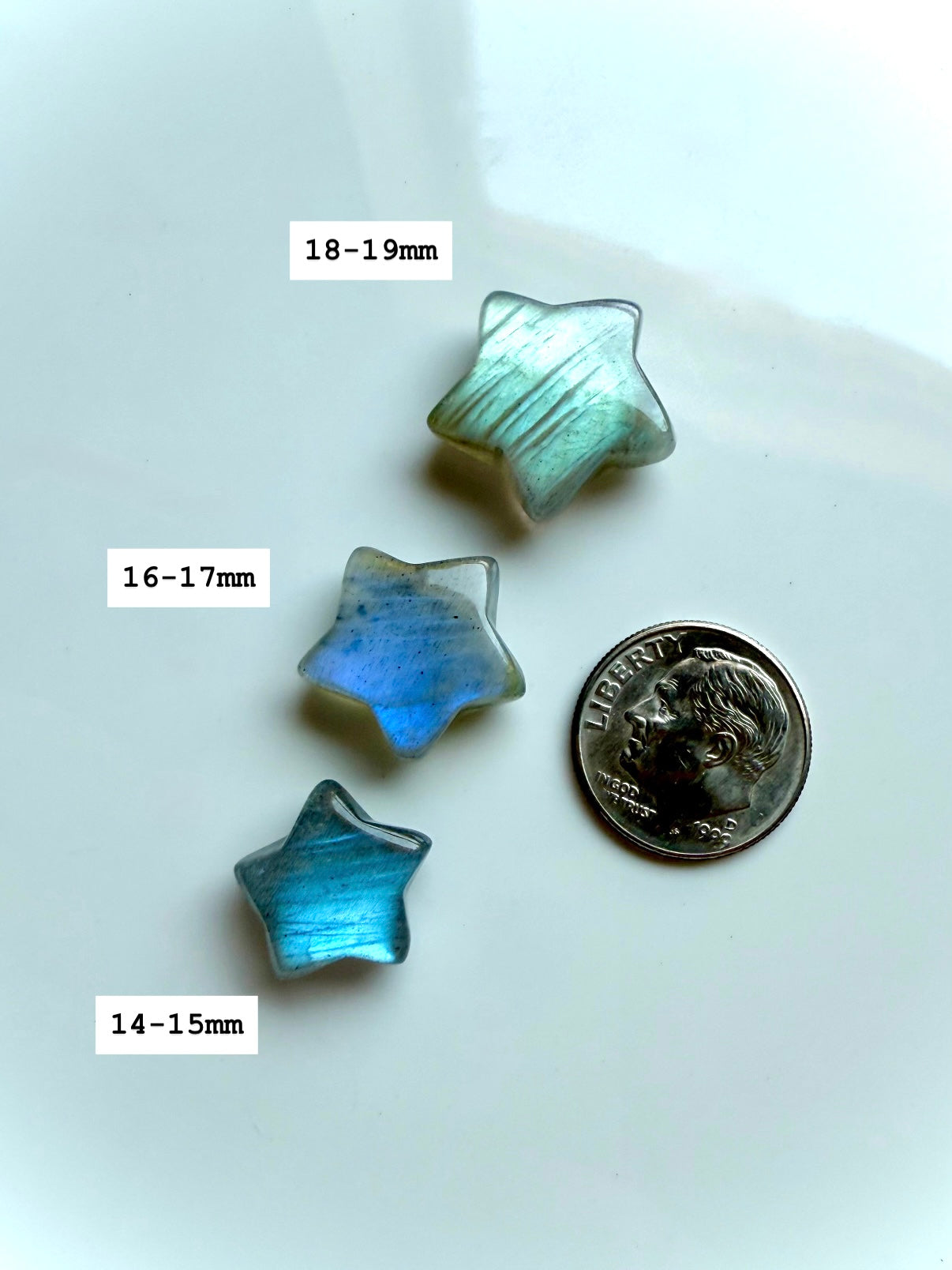 Three pastel Labradorite star carvings next to a quarter with sizes marked — micro crystal stars for chakra healing, display, or gifting.