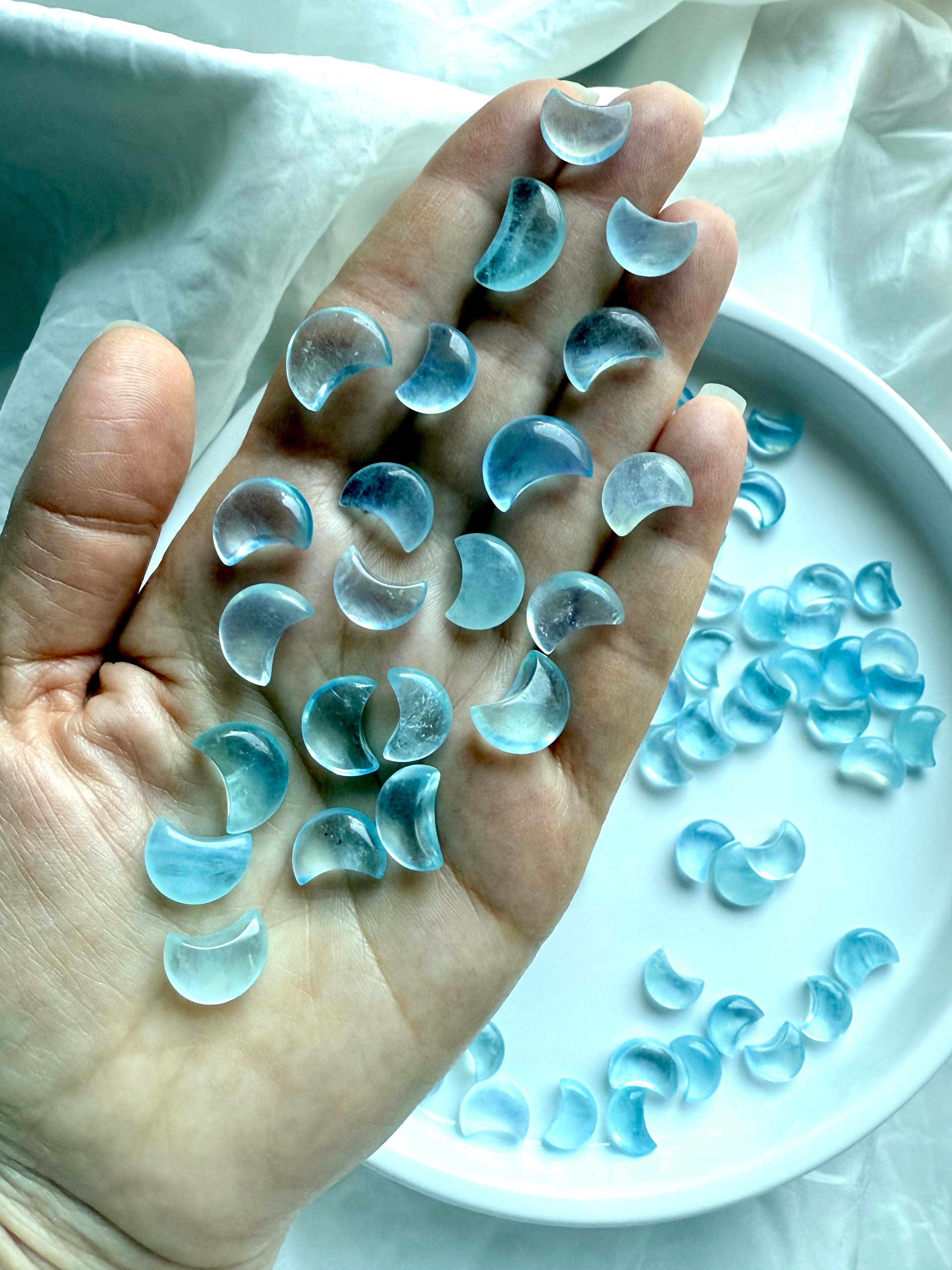 A hand holding a cascade of Aquamarine crescent moons, showing soft color variation, clarity, and polished shine