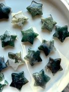 Assortment of polished Moss Agate stars on display tray, featuring deep forest green patterns and druzy-like inclusions — grounding crystal carving for heart chakra balance.