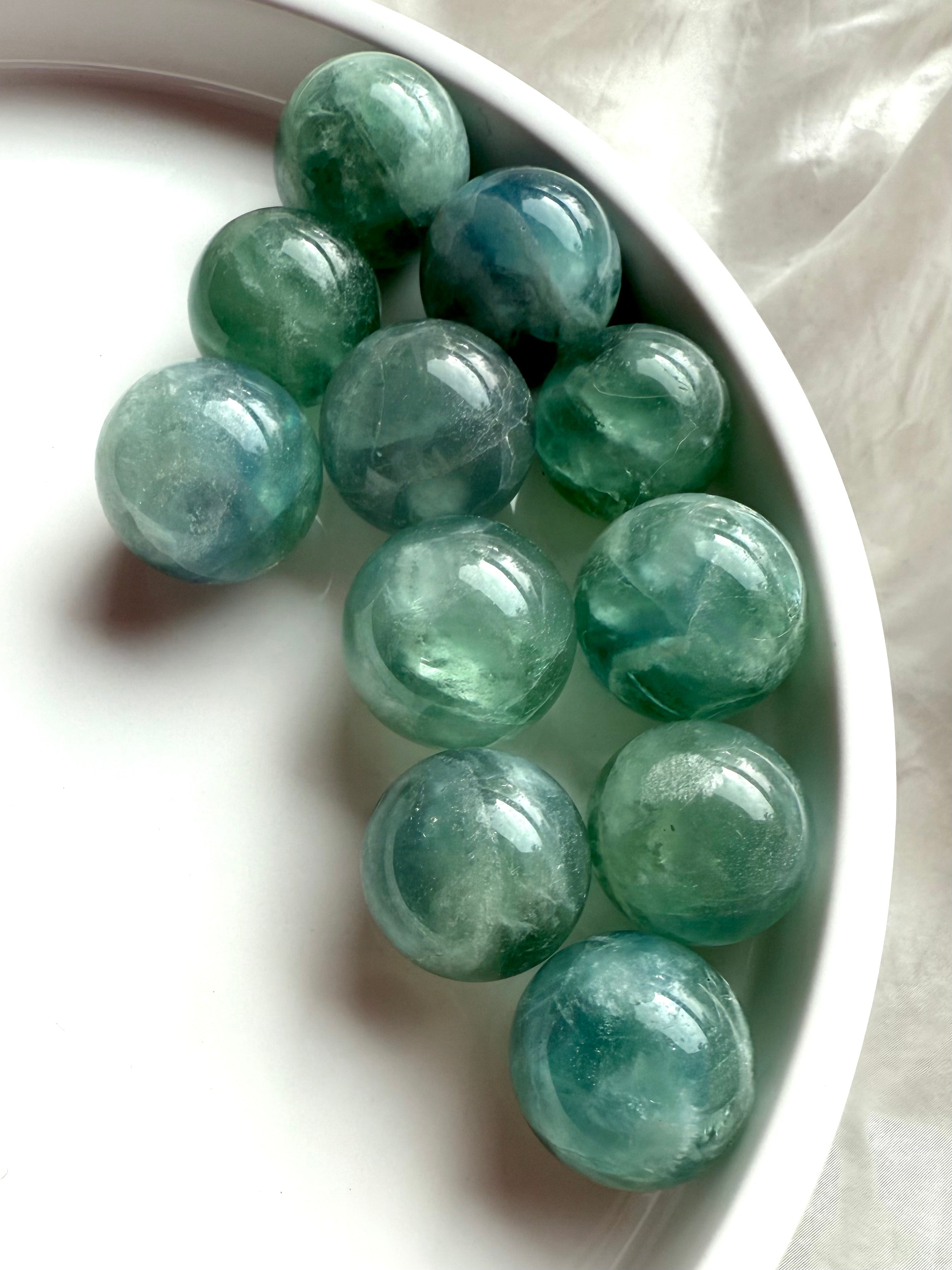 Mini teal Fluorite spheres with blue-green hues arranged on a white tray, healing crystals for clarity and Third Eye activation.