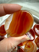 Polished Carnelian worry stone with translucent golden-orange and red banding held between fingers