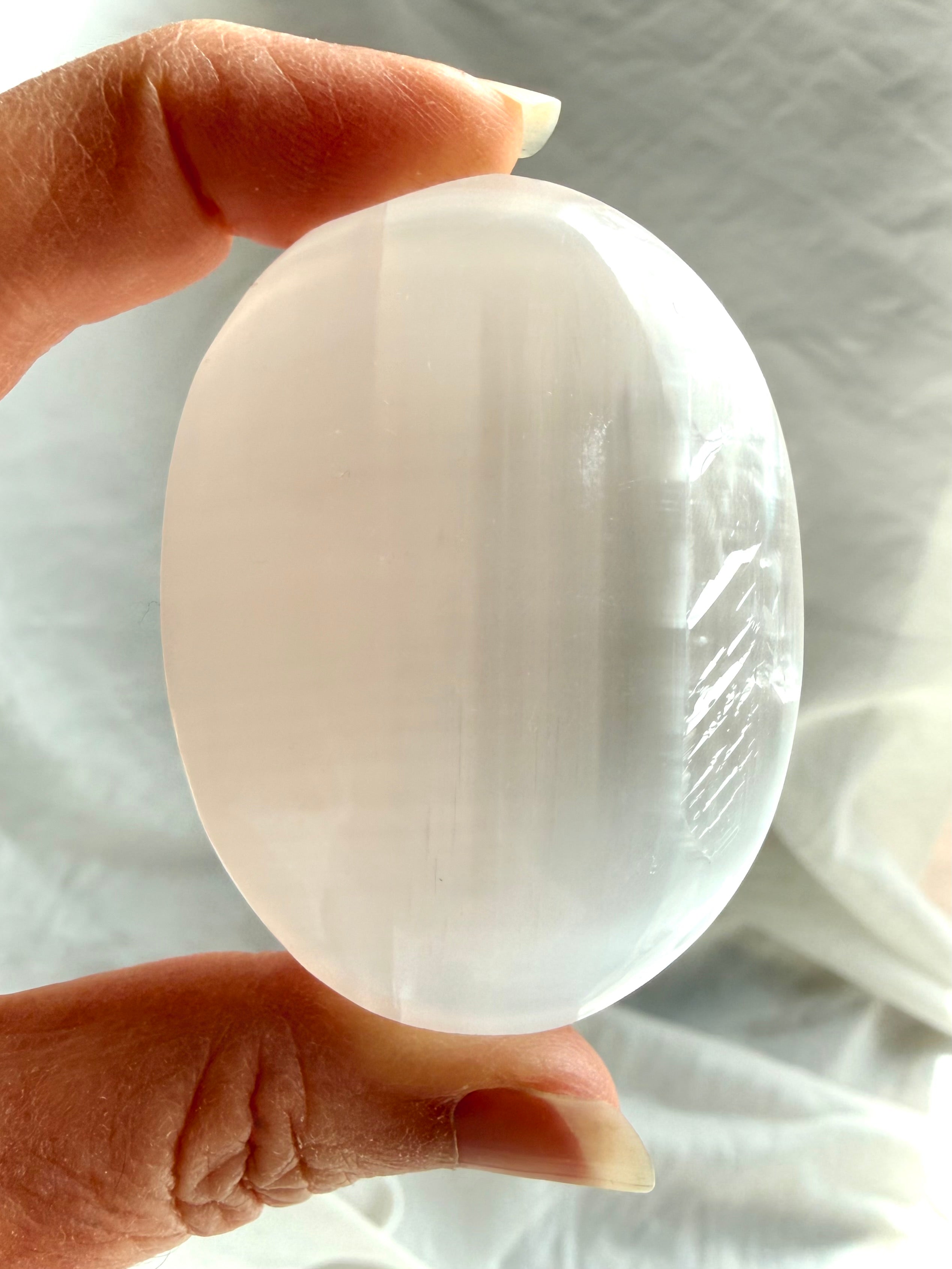 Close-up of polished Selenite palm stone showing silky translucency, luminous glow, and natural satin spar patterning